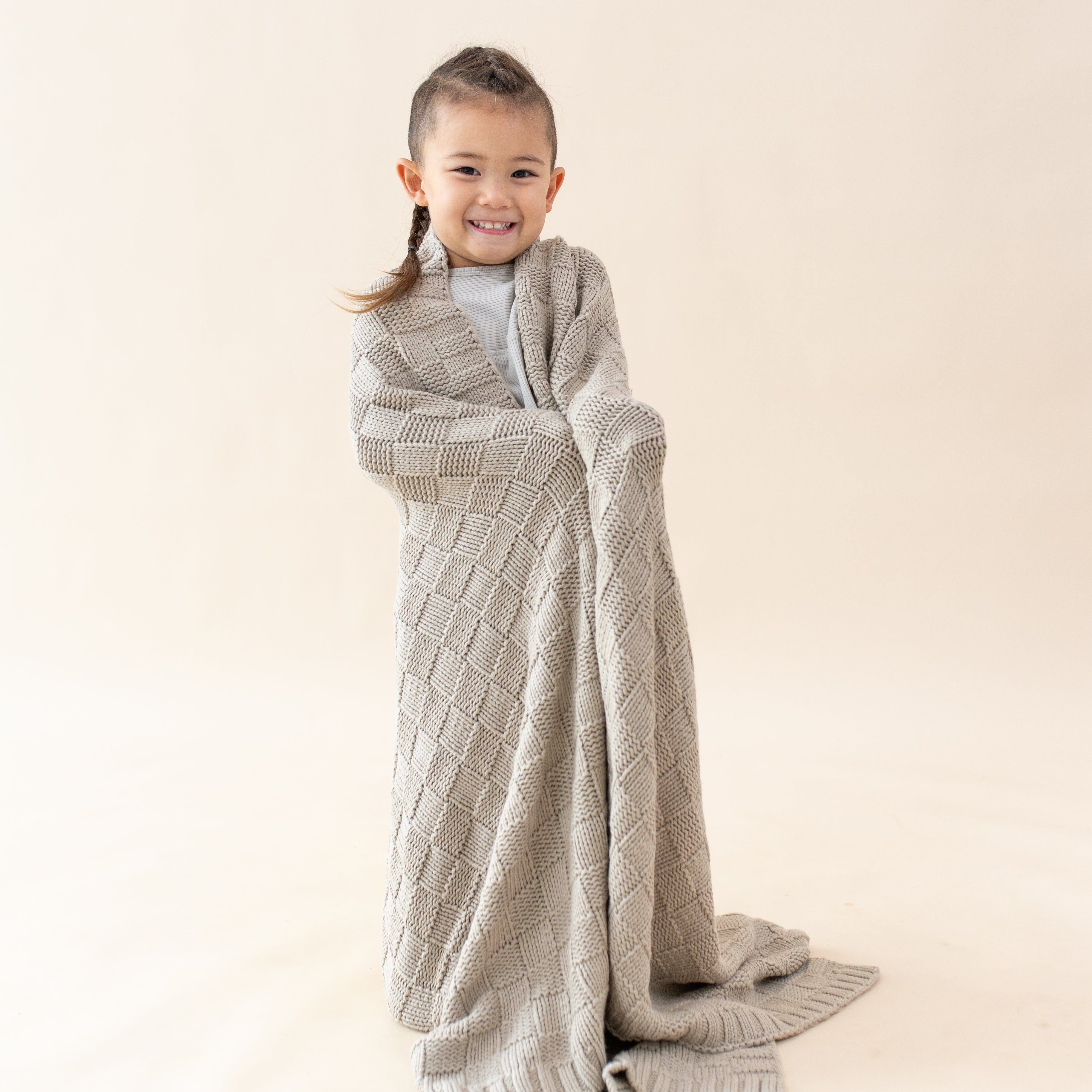 Girl wrapped in cozy Kyte Baby Chunky Knit Basket Weave Toddler Blanket in Almond neutral