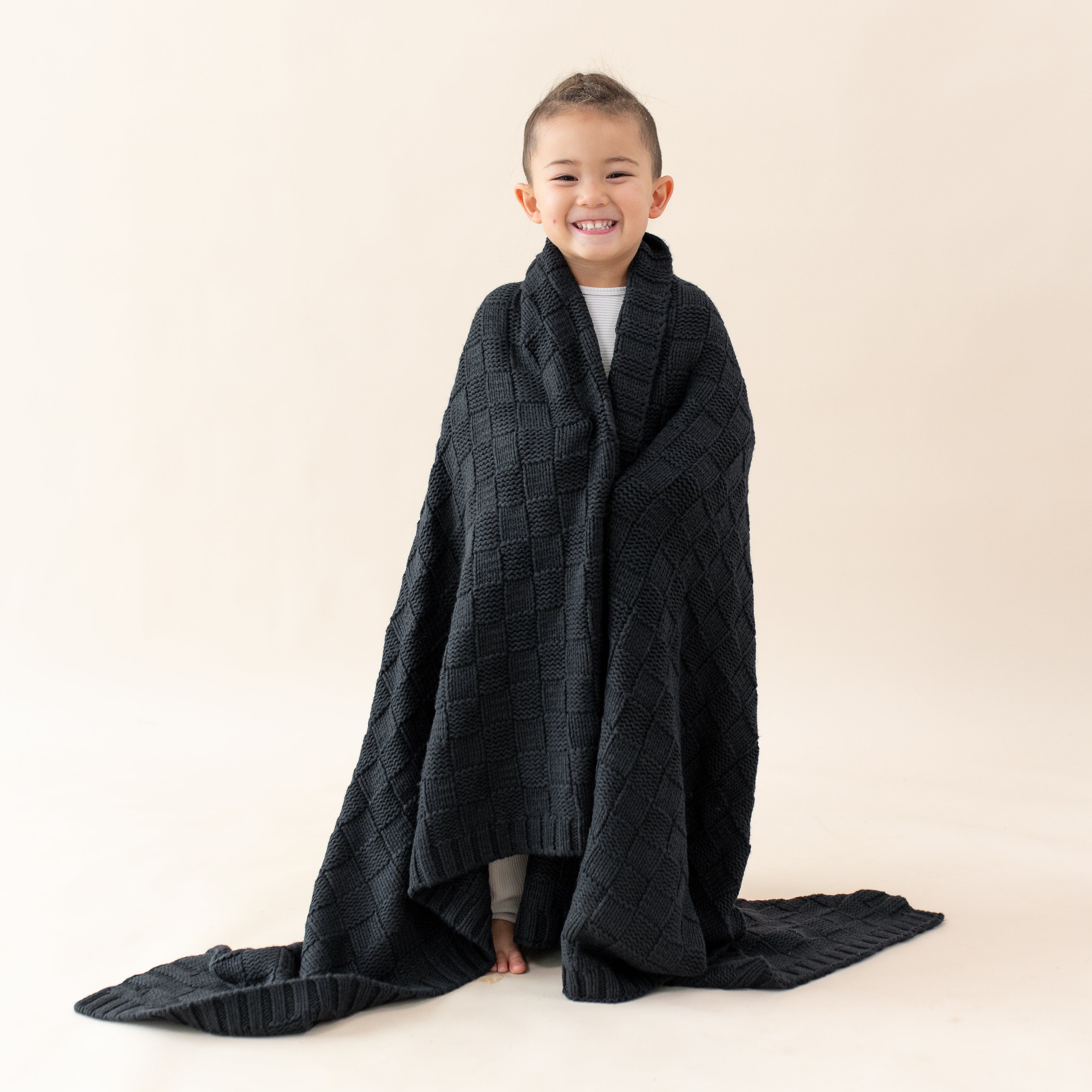 Girl wrapped in Kyte Baby Chunky Knit Basket Weave Toddler Blanket in Midnight black