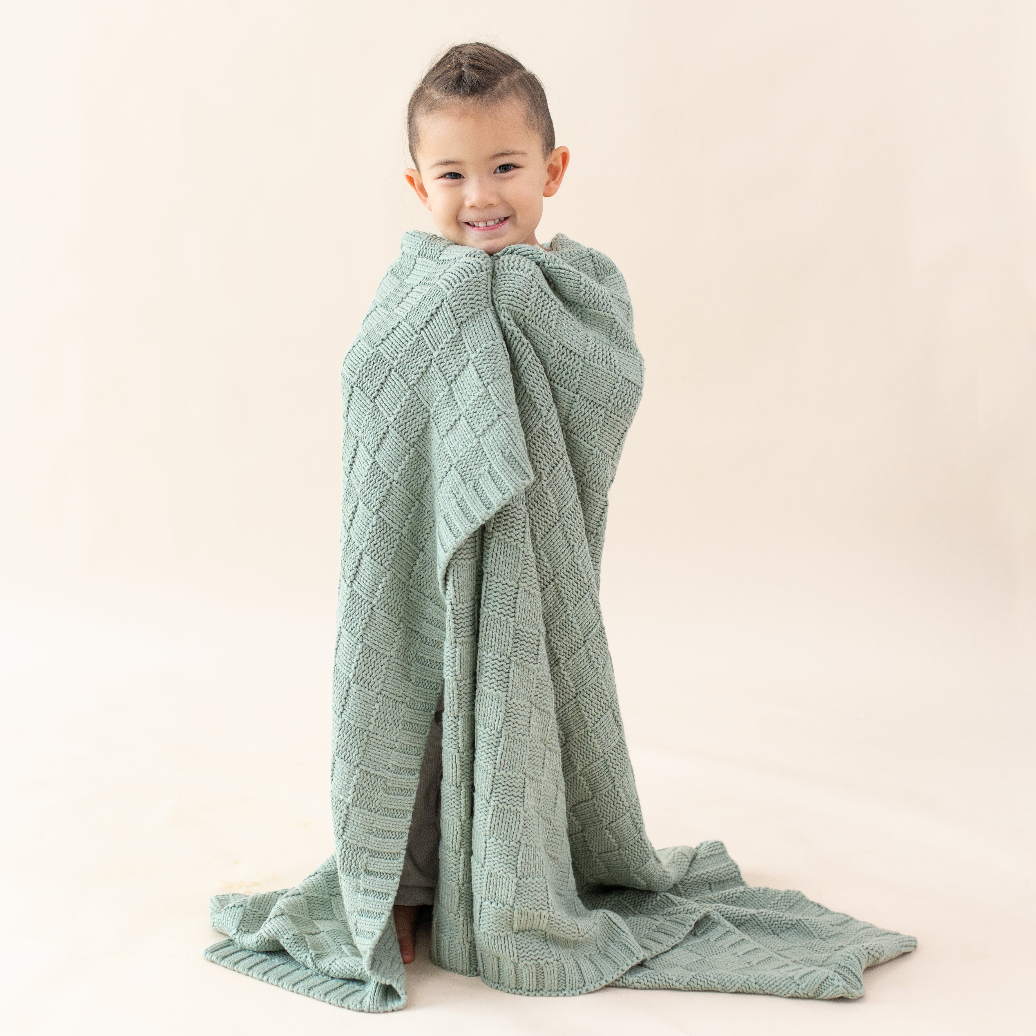 Girl wrapped in Kyte Baby Chunky Knit Basket Weave Toddler Blanket in Thyme