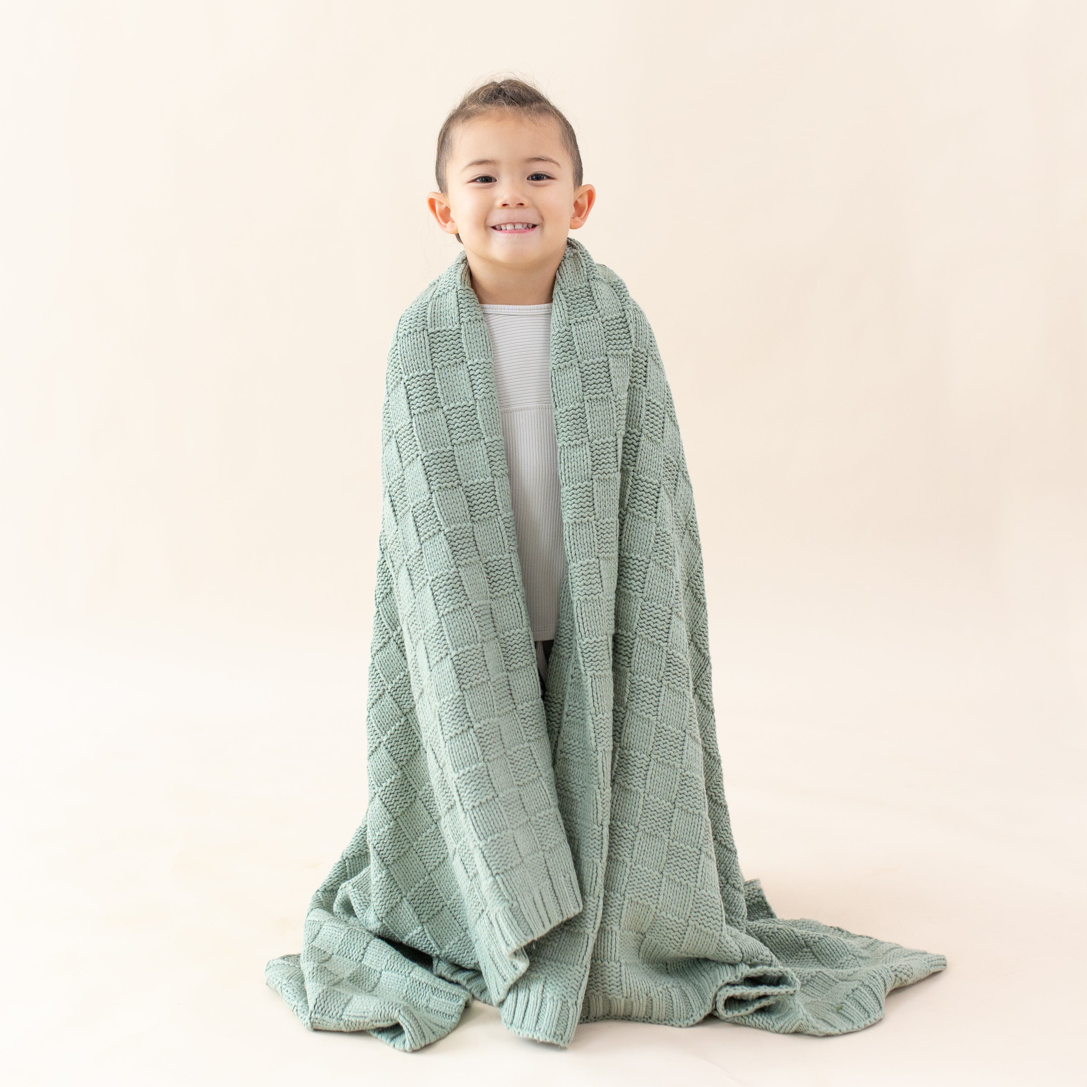 Girl wrapped in cozy Kyte Baby Chunky Knit Basket Weave Toddler Blanket in Thyme green