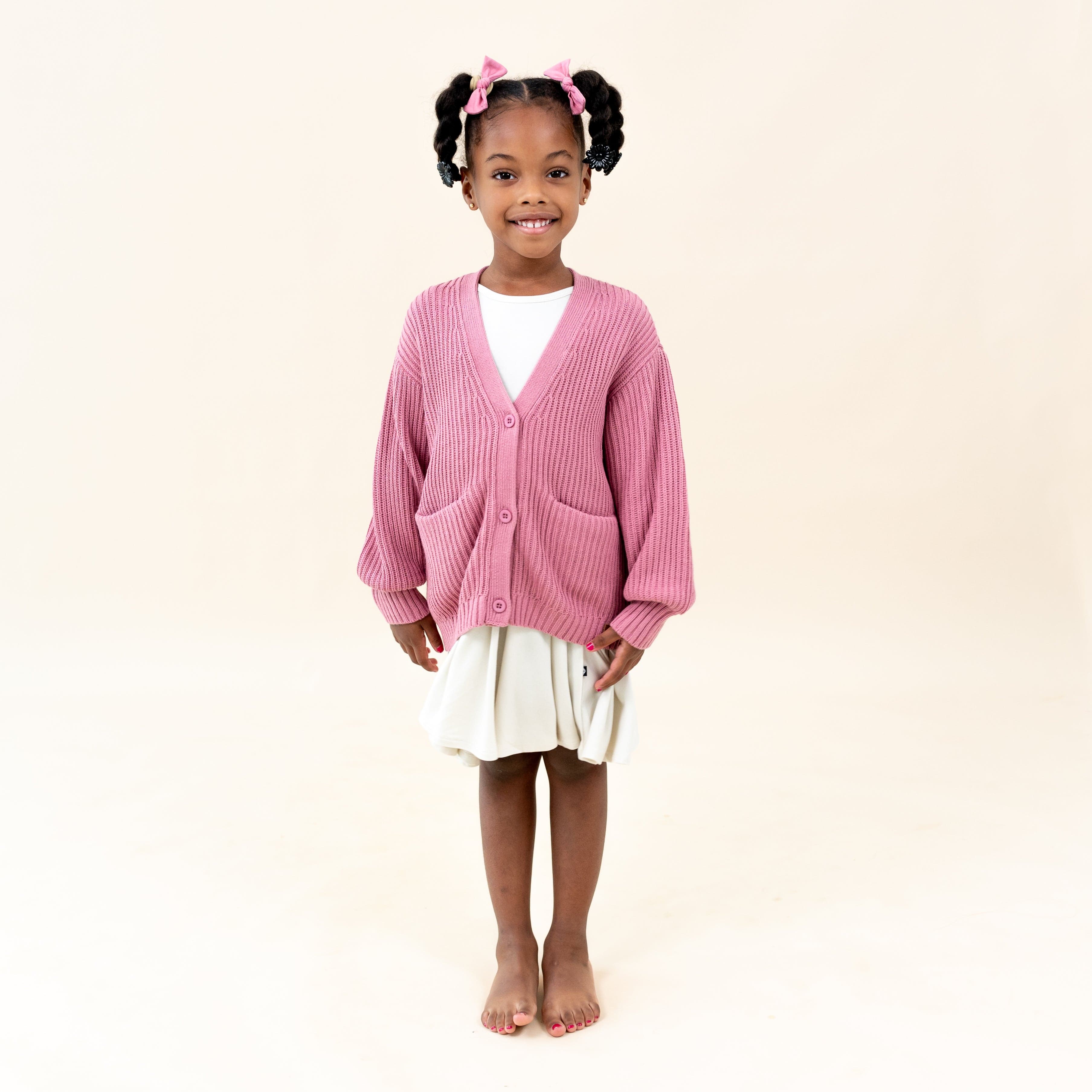 Child wearing Kyte Baby Chunky Knit Oversized Cardigan with front pockets in Apple Blossom pink