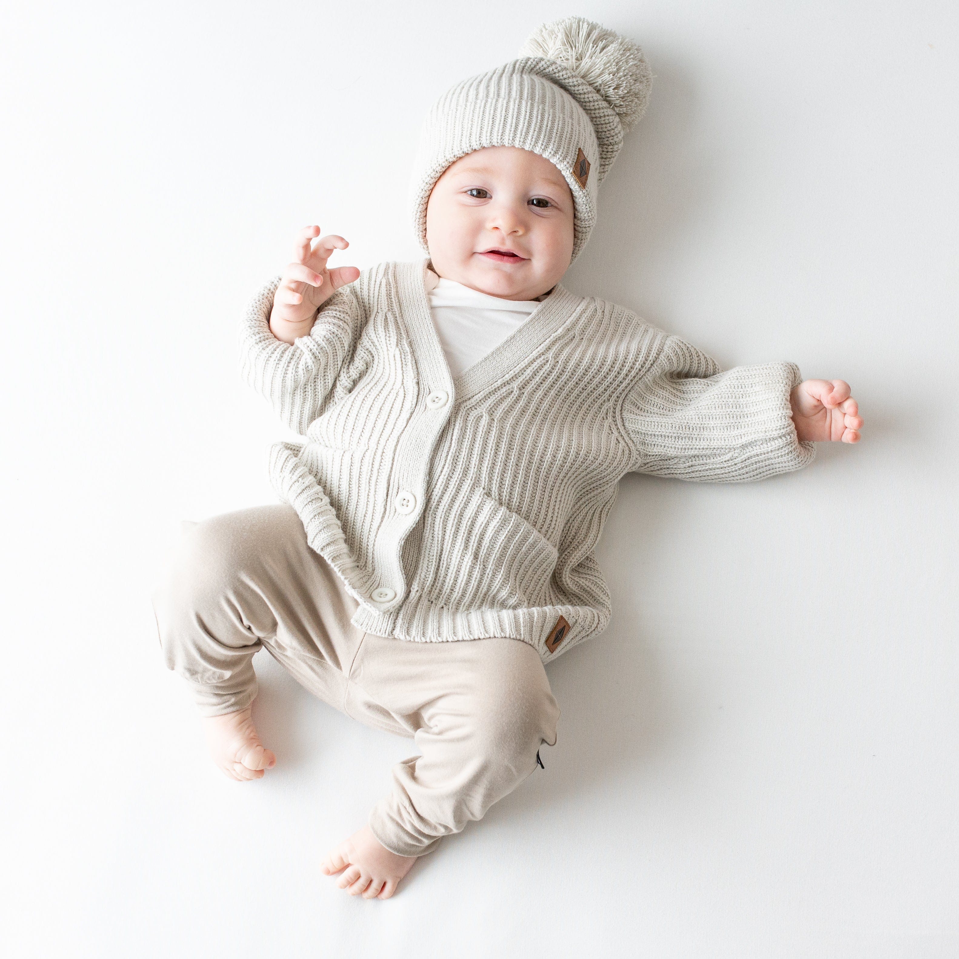Infant wearing Kyte Baby Chunky Knit Oversized Cardigan with front pockets in Oat