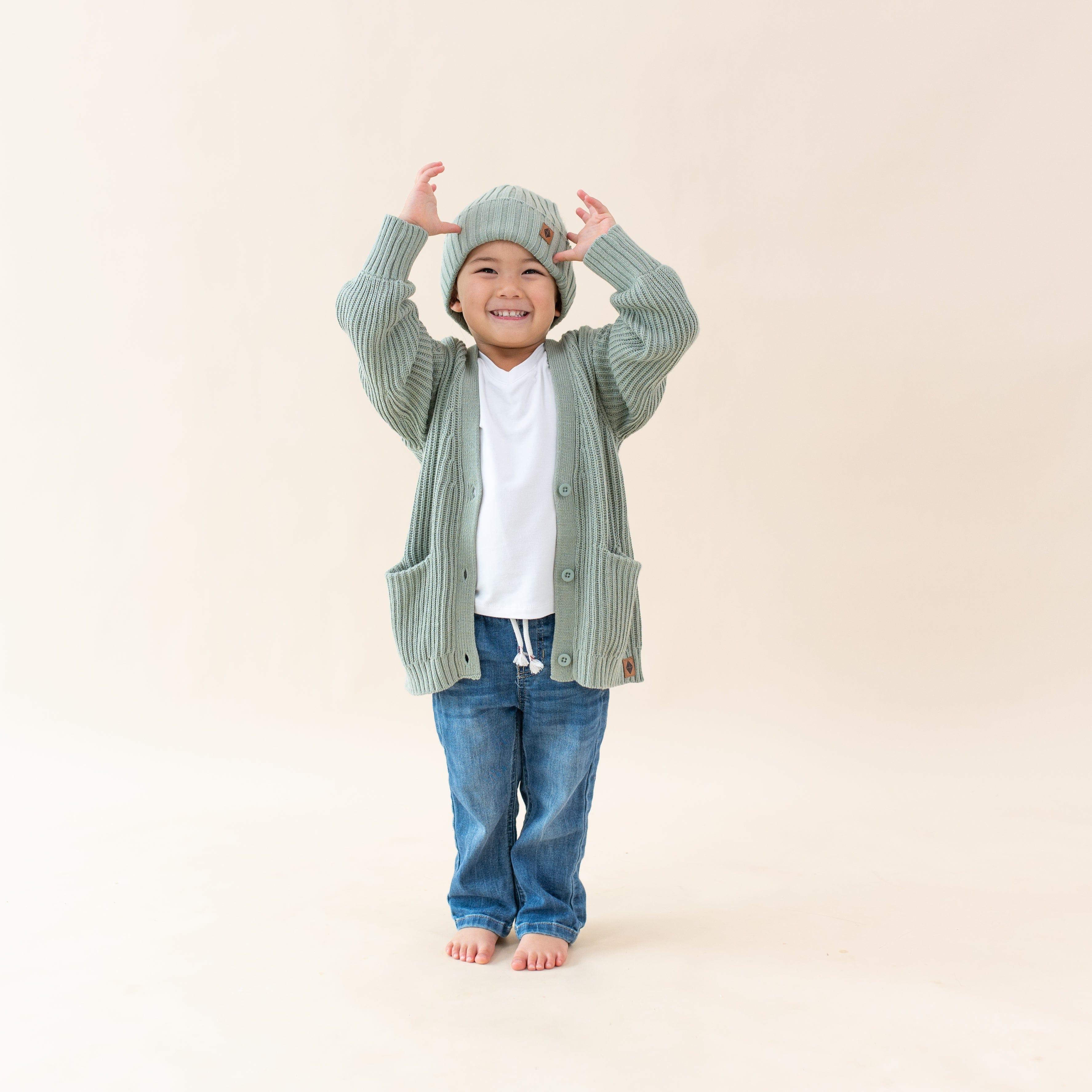 Child wearing Kyte Baby Chunky Knit Oversized Cardigan with front pockets in Thyme green
