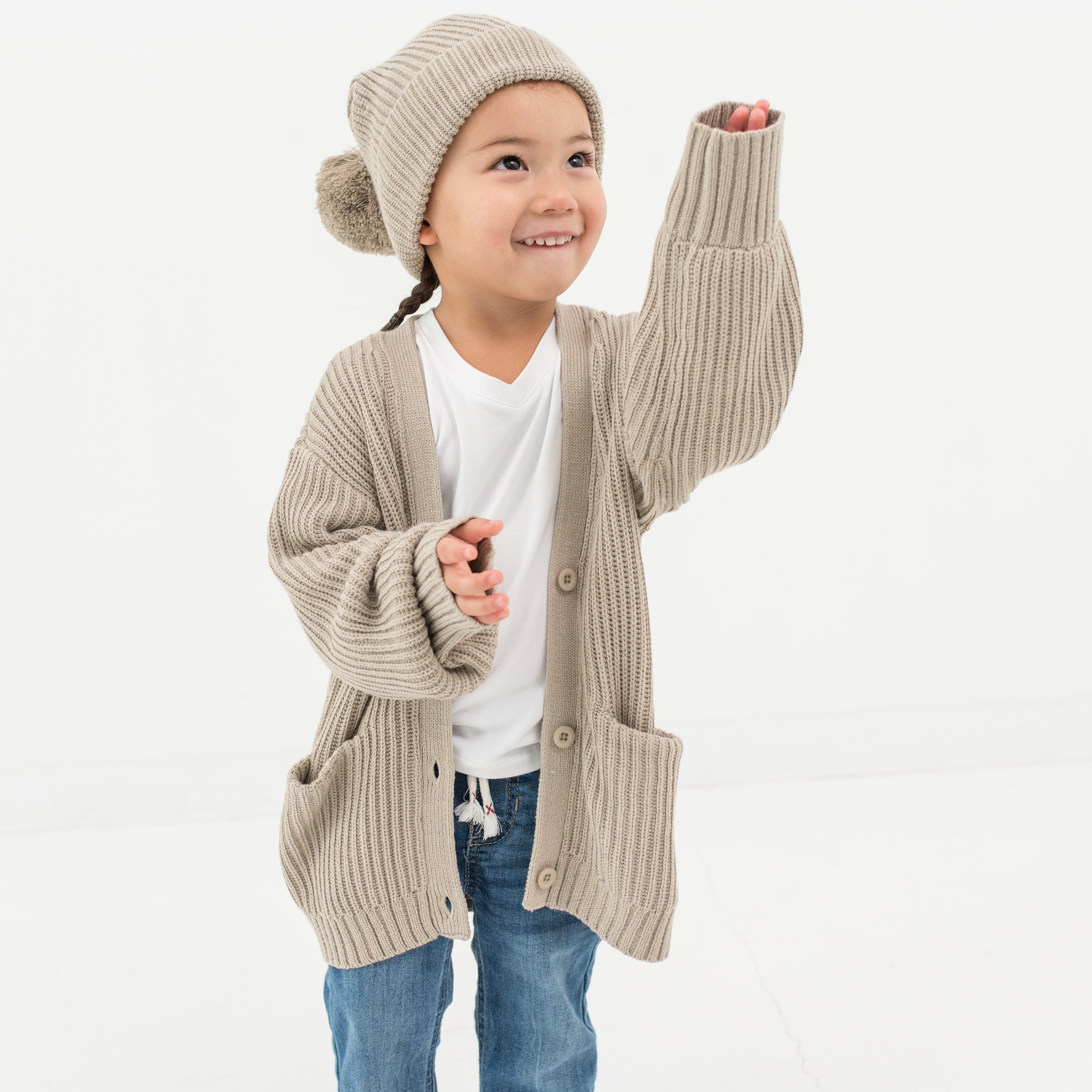 Child wearing soft and stretchy Kyte Baby Chunky Knit Pom Beanie in Almond