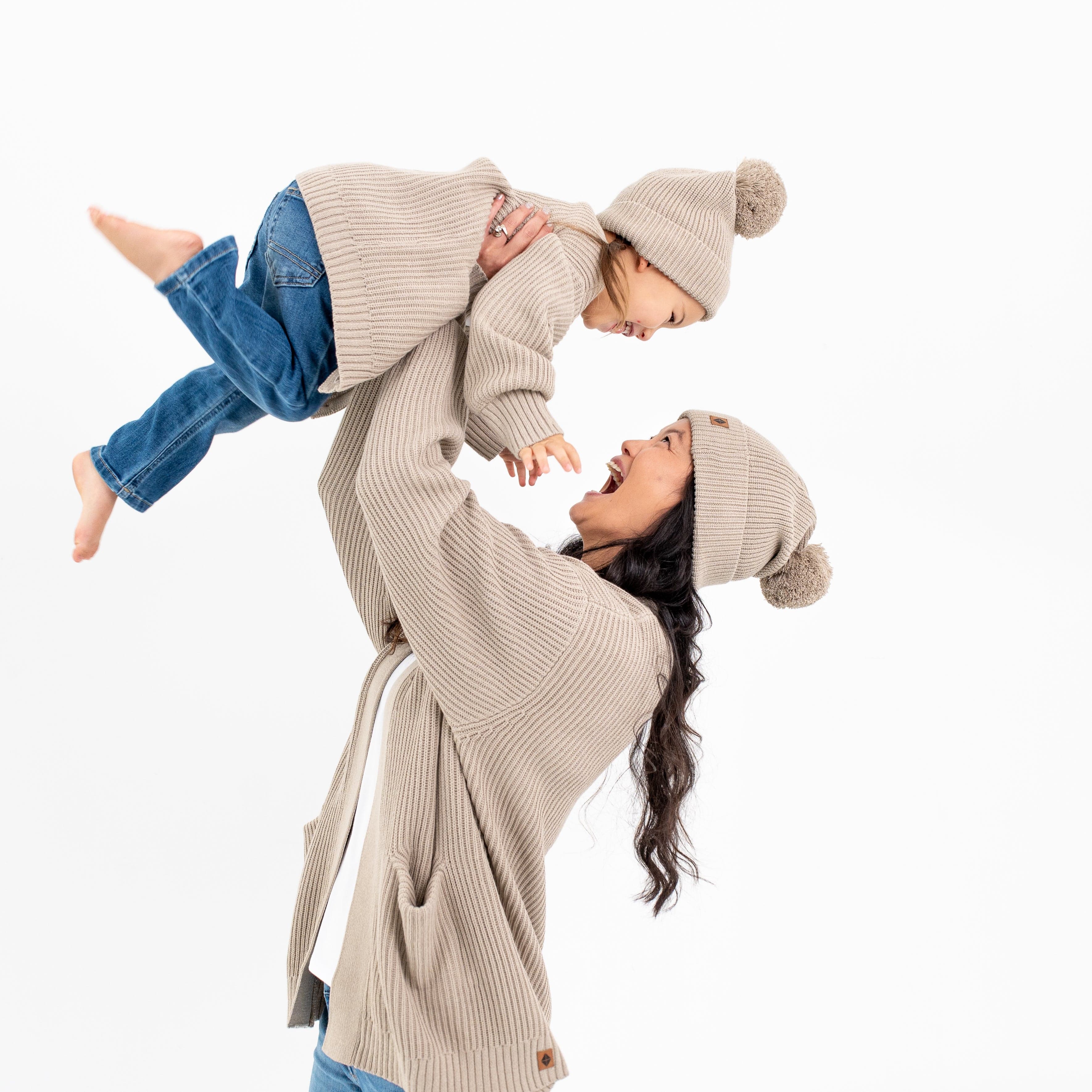 Mom and child wearing matching Kyte Baby Chunky Knit Pom Beanies in Almond