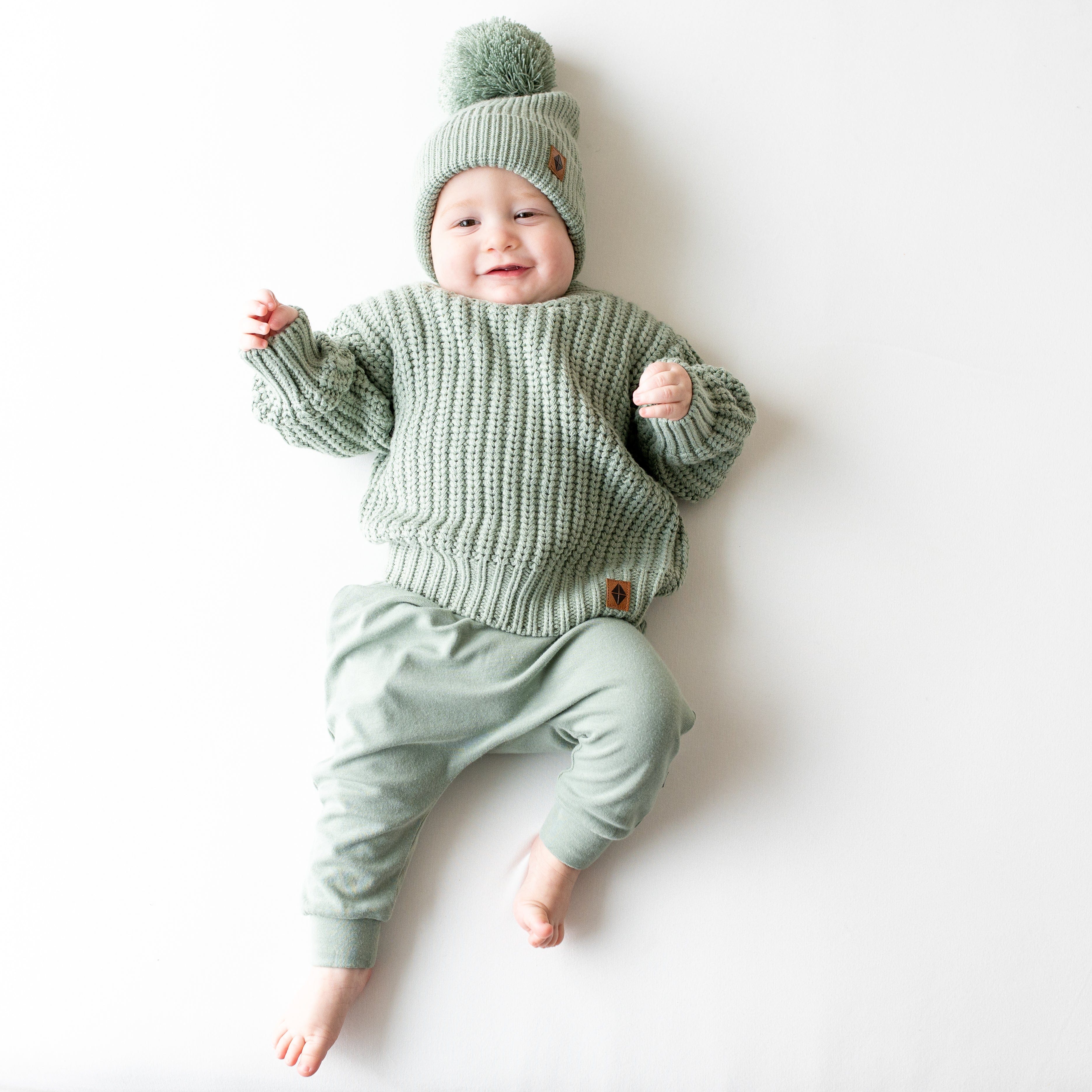 Infant wearing soft and stretchy Kyte Baby Chunky Knit Pom Beanie in Thyme green