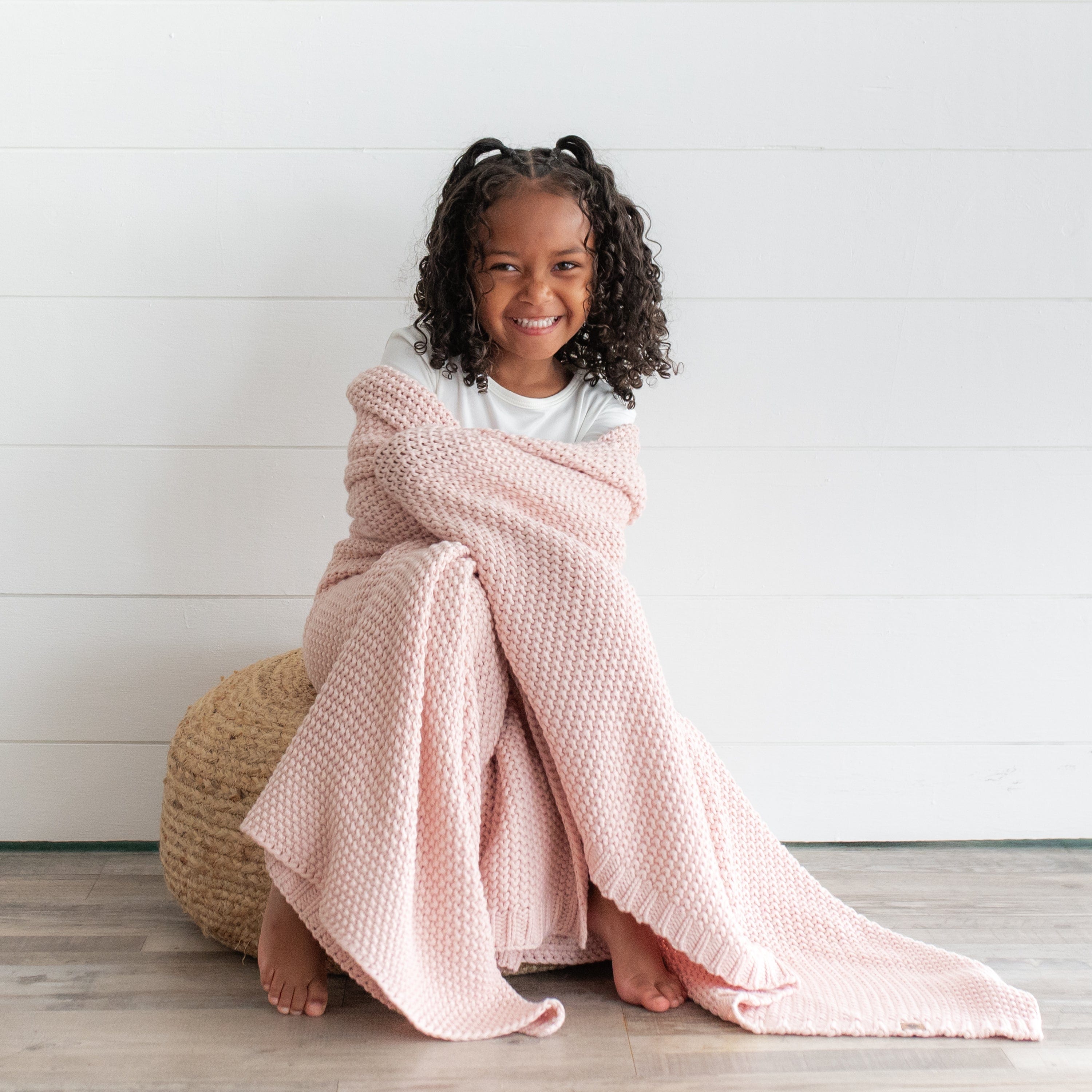 Girl wrapped in Kyte Baby Chunky Knit Toddler Blanket in Blush
