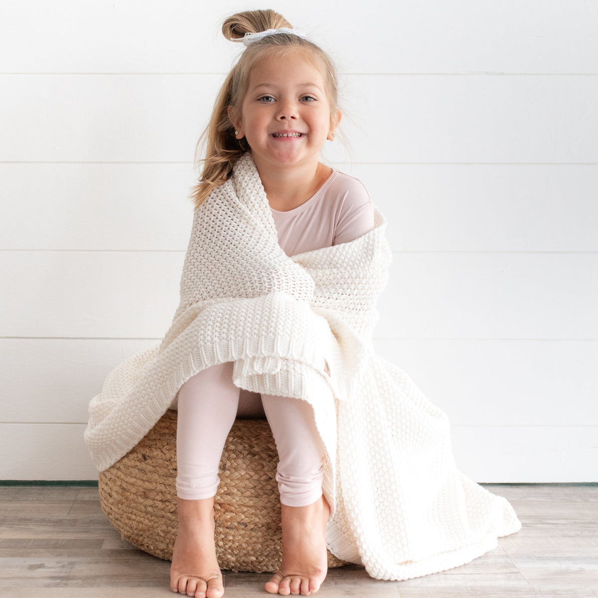 Girl wrapped in Kyte Baby Chunky Knit Toddler Blanket in Cloud