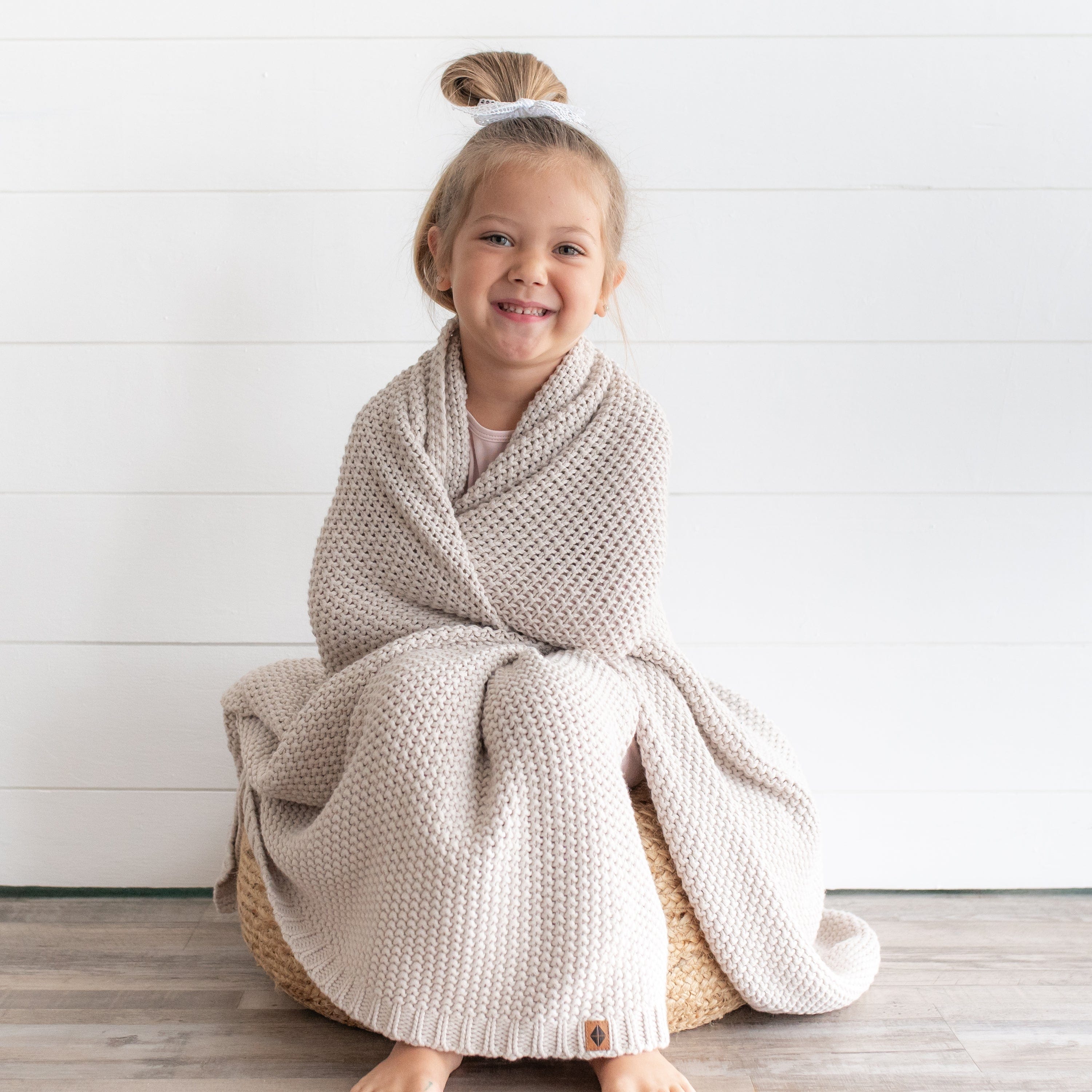 Girl wrapped in Kyte Baby Chunky Knit Toddler Blanket in Oat