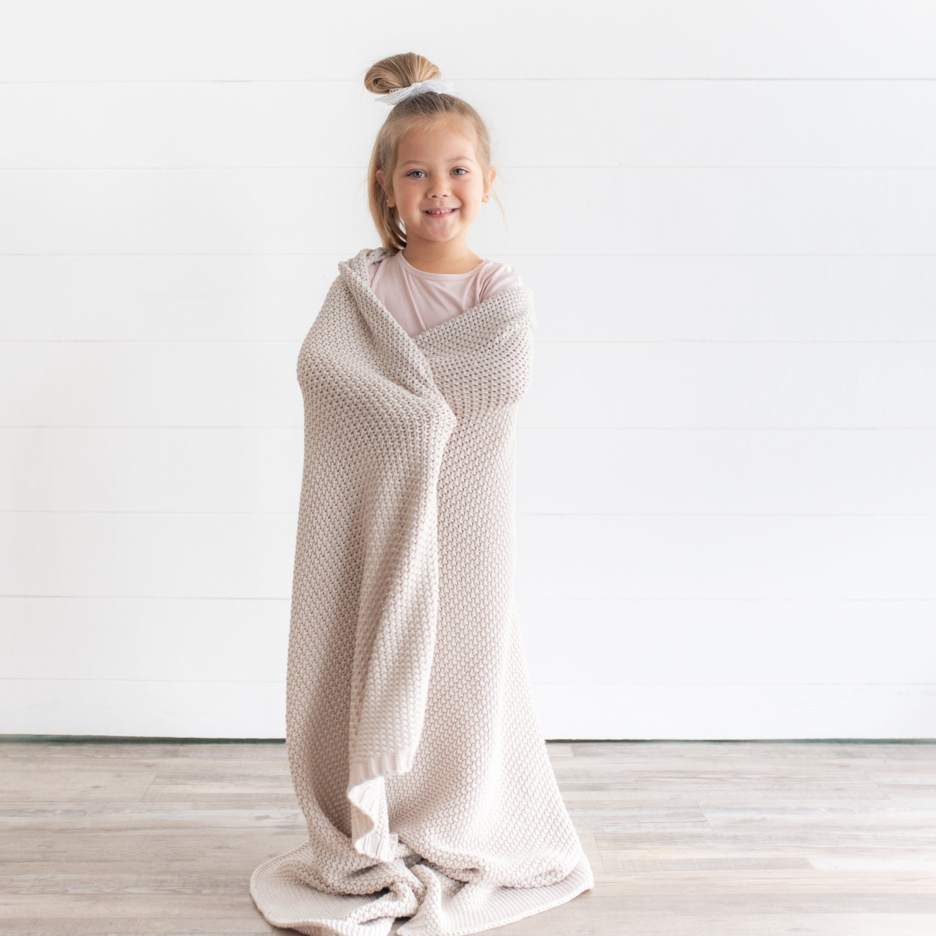 Girl wrapped in Kyte Baby bamboo Chunky Knit Toddler Blanket in Oat