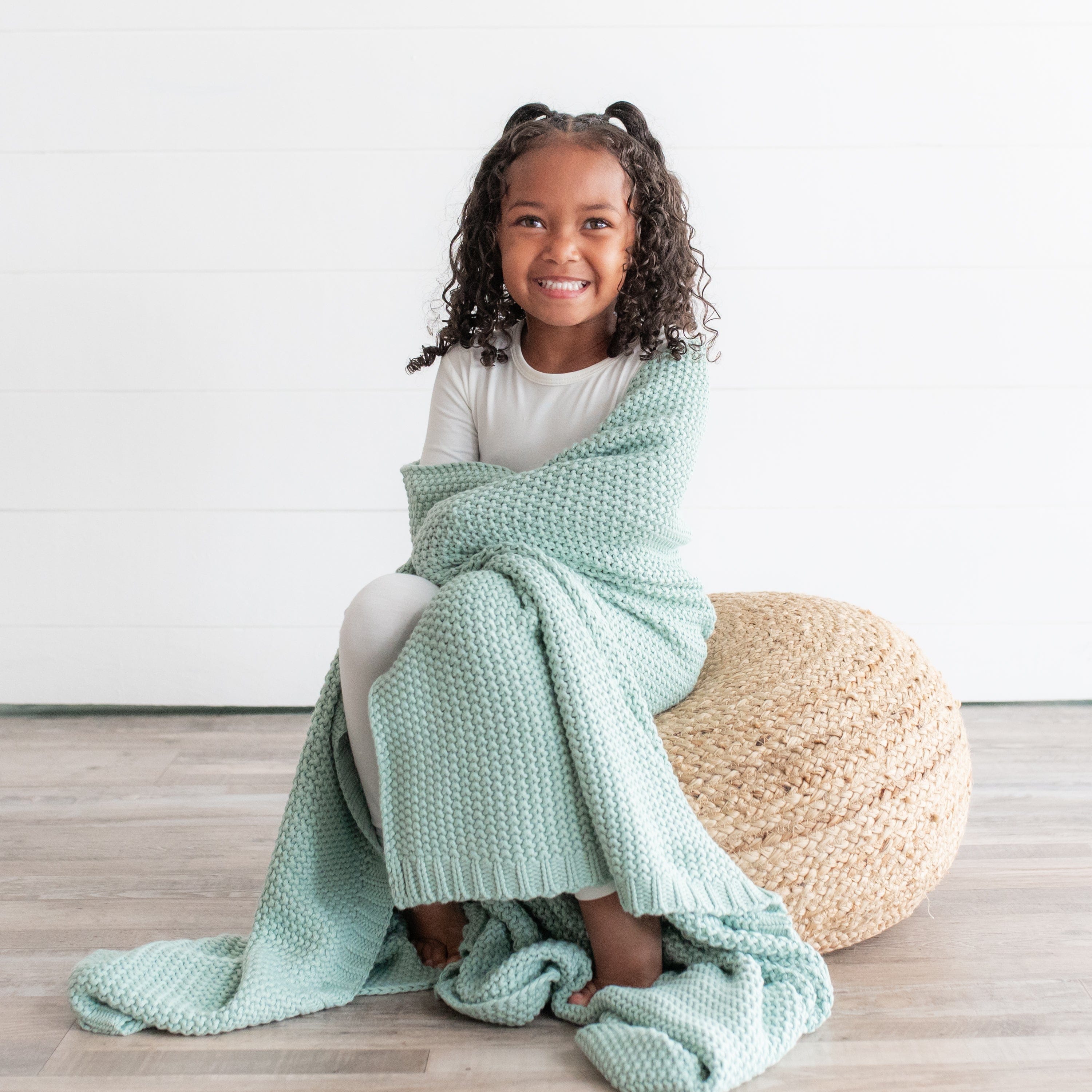 Girl wrapped in Kyte Baby Chunky Knit Toddler Blanket in Sage