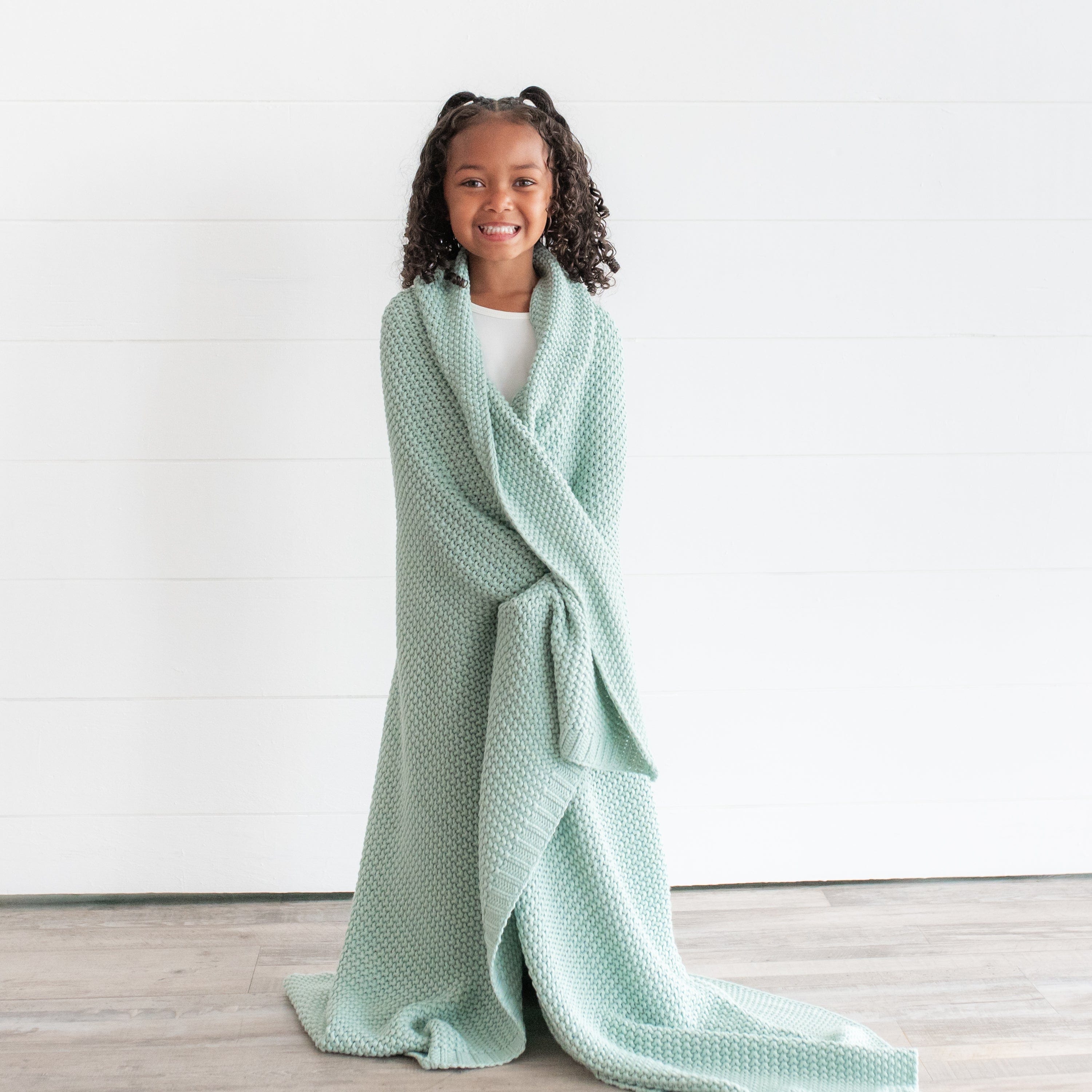 Child wrapped in Kyte Baby Chunky Knit Toddler Blanket in Sage Green