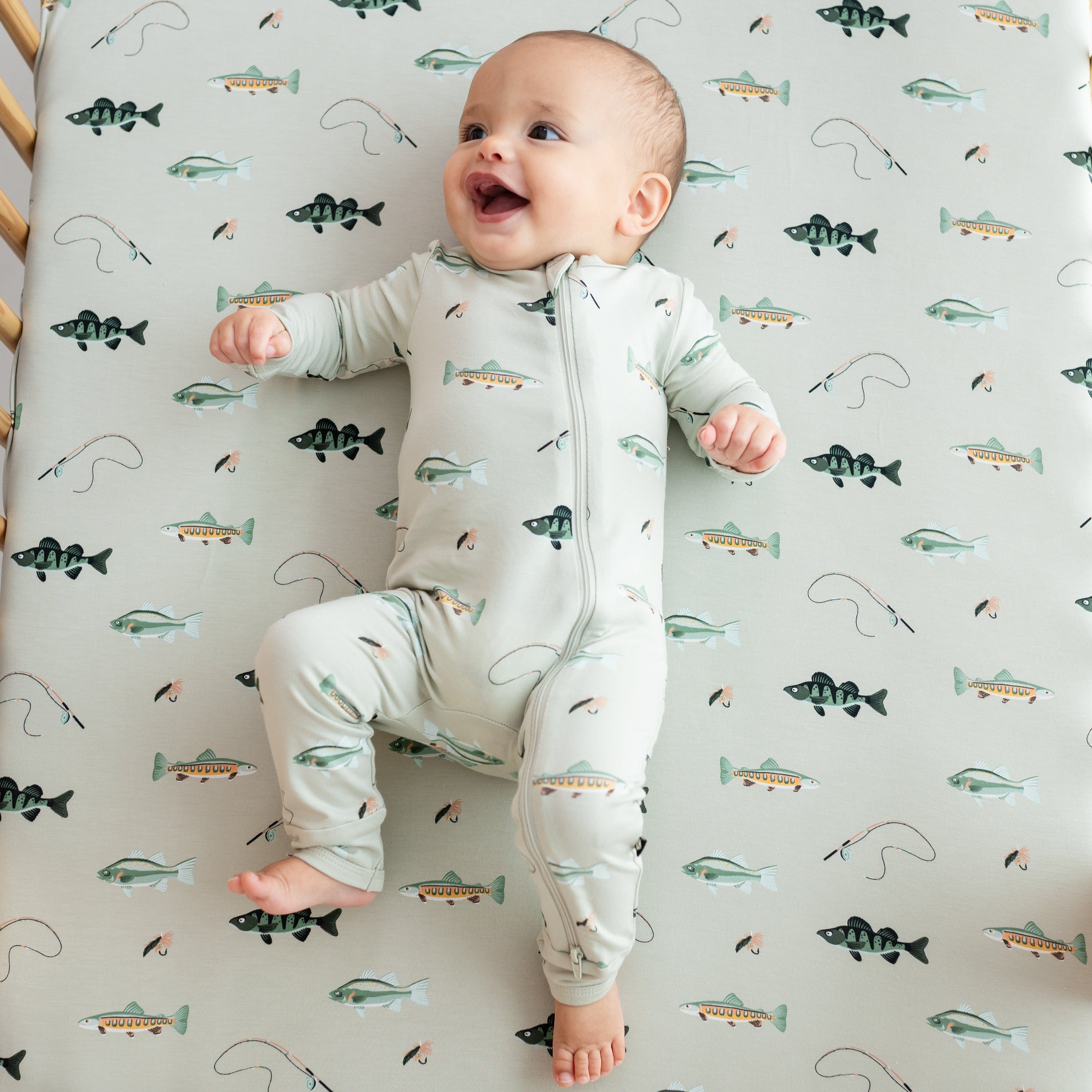 Smiling infant laying on a Fishing crib sheet wearing the Zippered Romper in Fishing