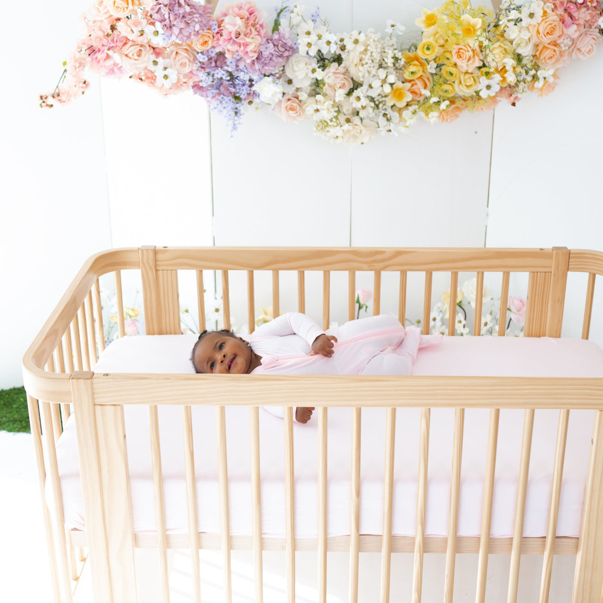 Infant laying on Kyte Baby Crib Sheet in Sakura pink
