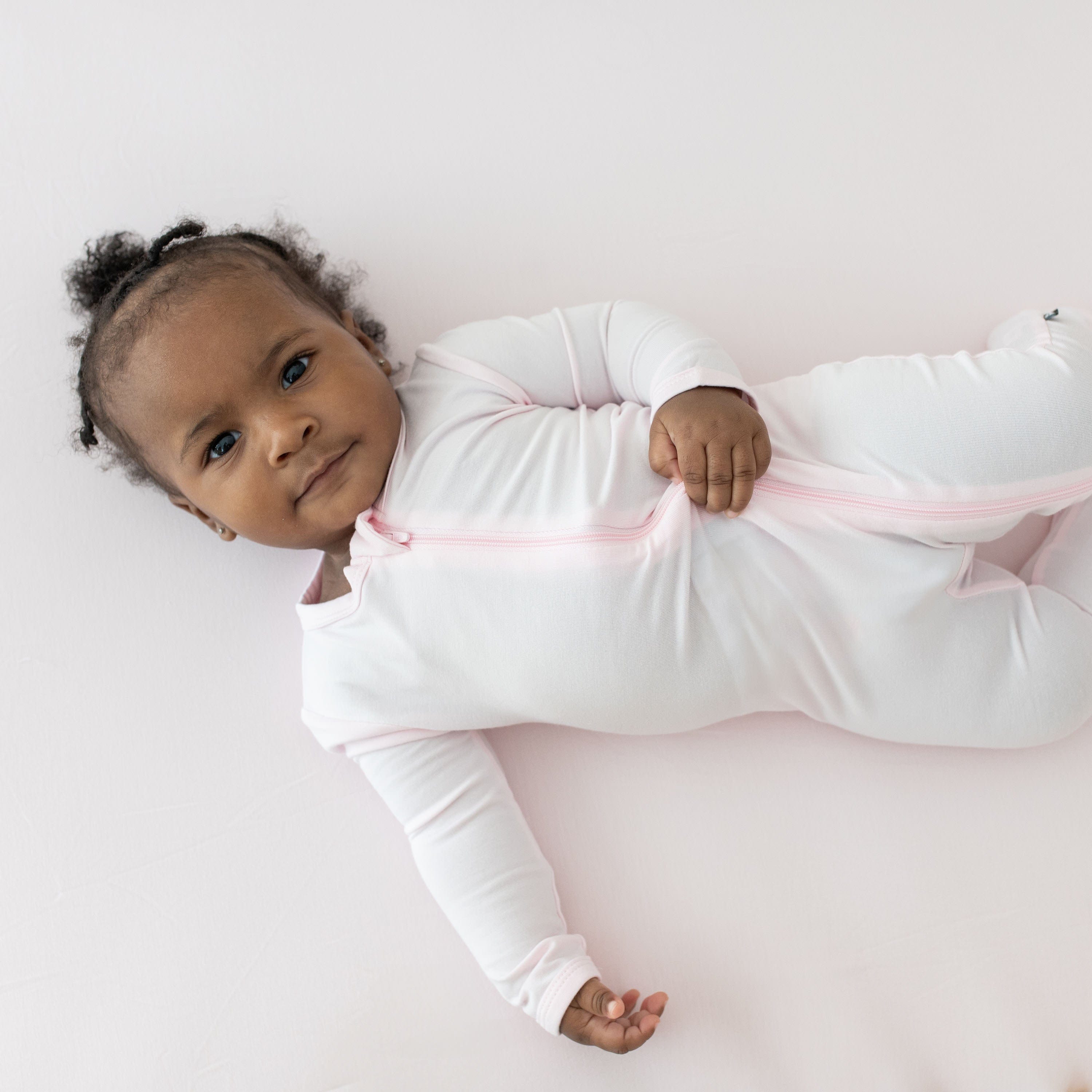 Infant laying on Kyte Baby bamboo Crib Sheet in Sakura