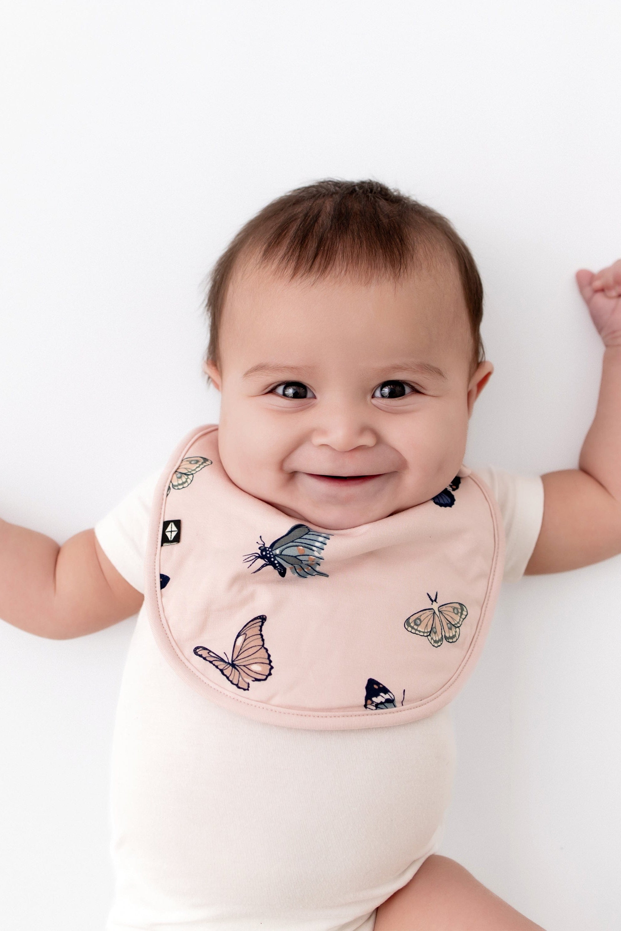 Infant wearing Kyte Baby Cushy Bib in Blush Butterfly