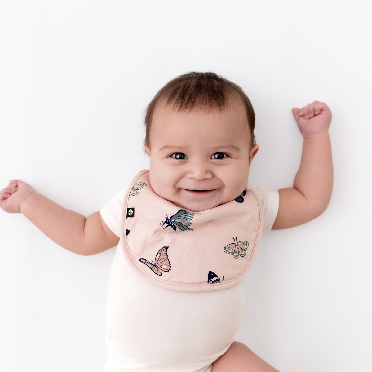 Infant wearing Kyte Baby Cushy Bib in Blush Butterfly