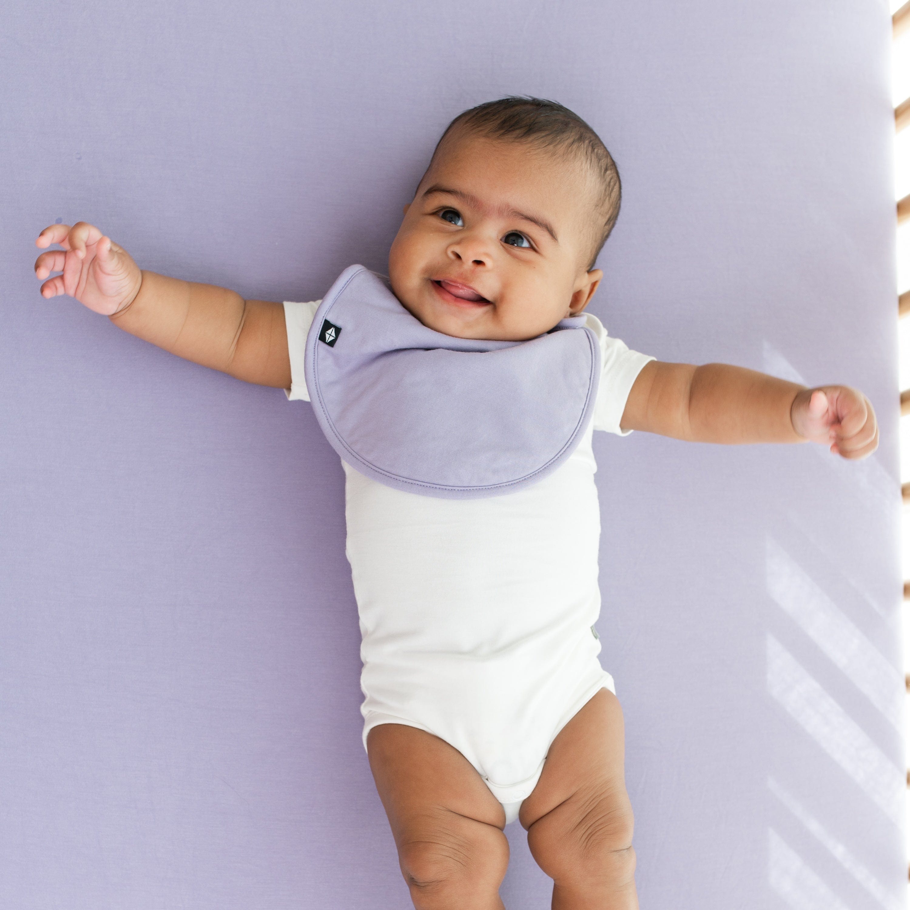 Infant wearing Kyte Baby Cushy Bib in Taro