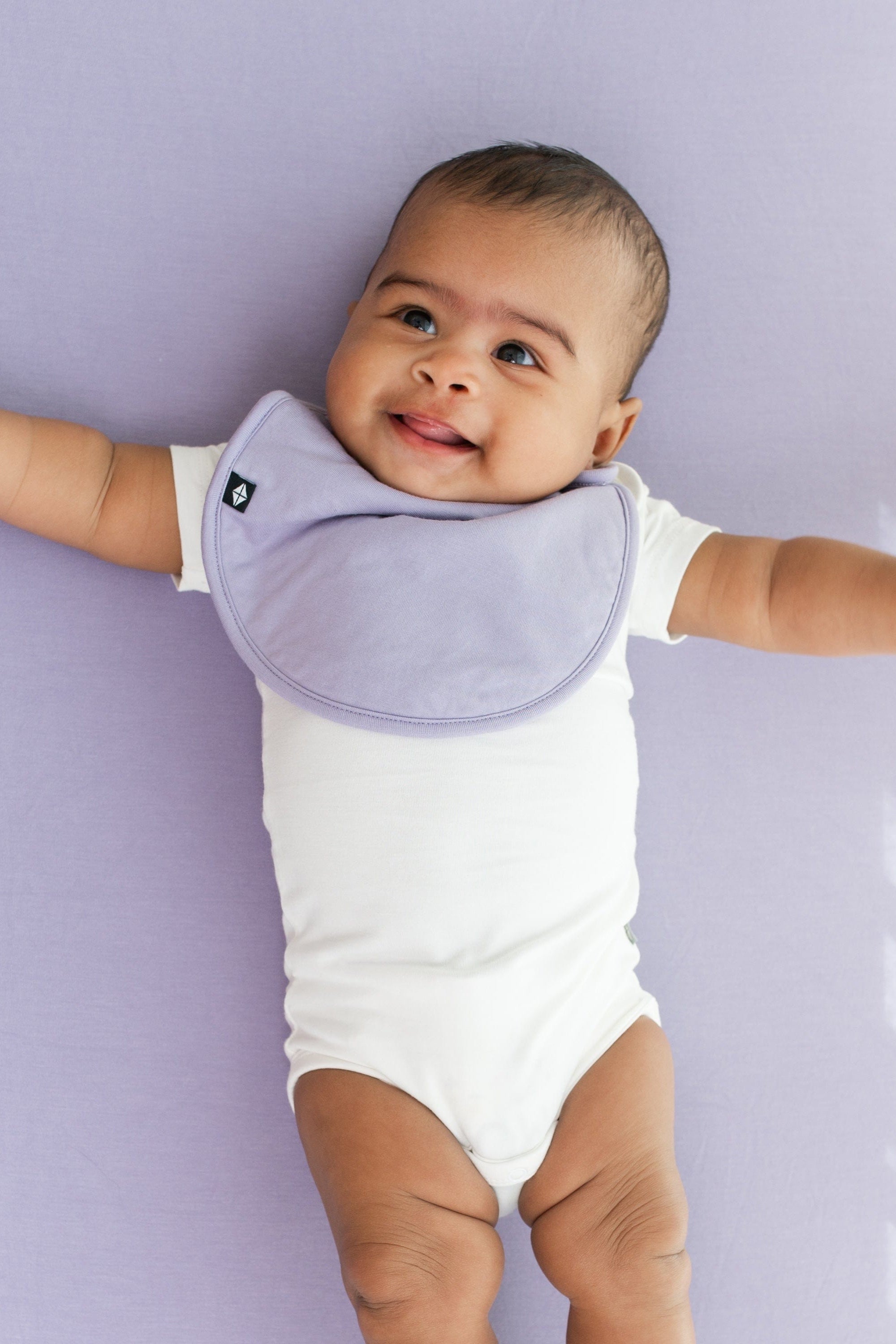 Infant wearing Kyte Baby Cushy Bib in Taro