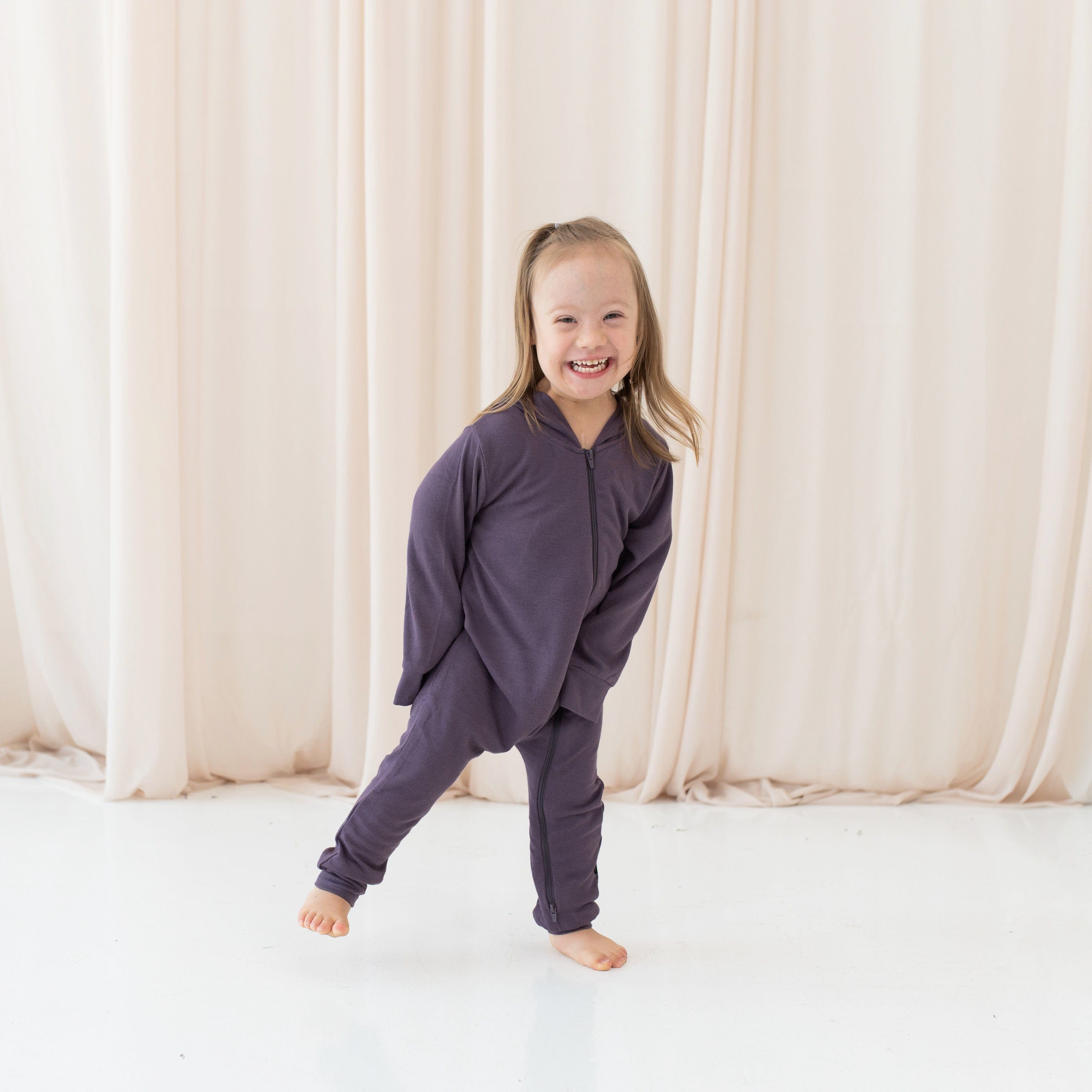 Girl wearing zippered purple romper with hood in Currant