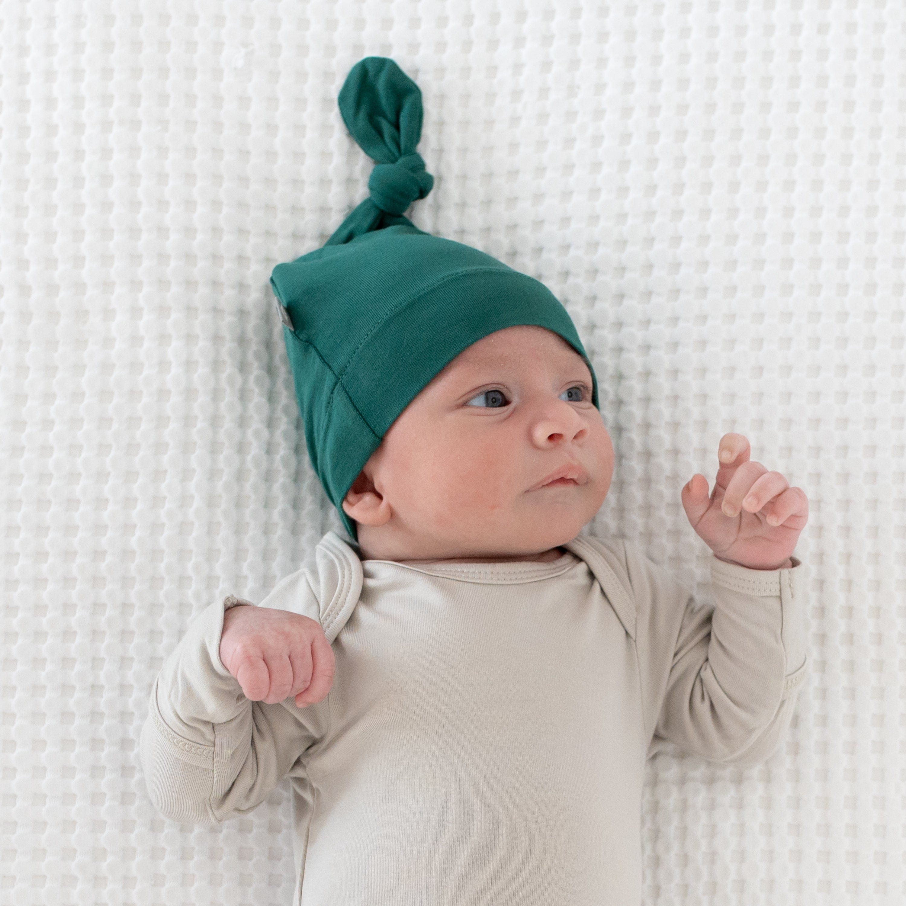 Newborn laying on a blanket while wearing a Kyte Baby Knotted Cap in Emerald