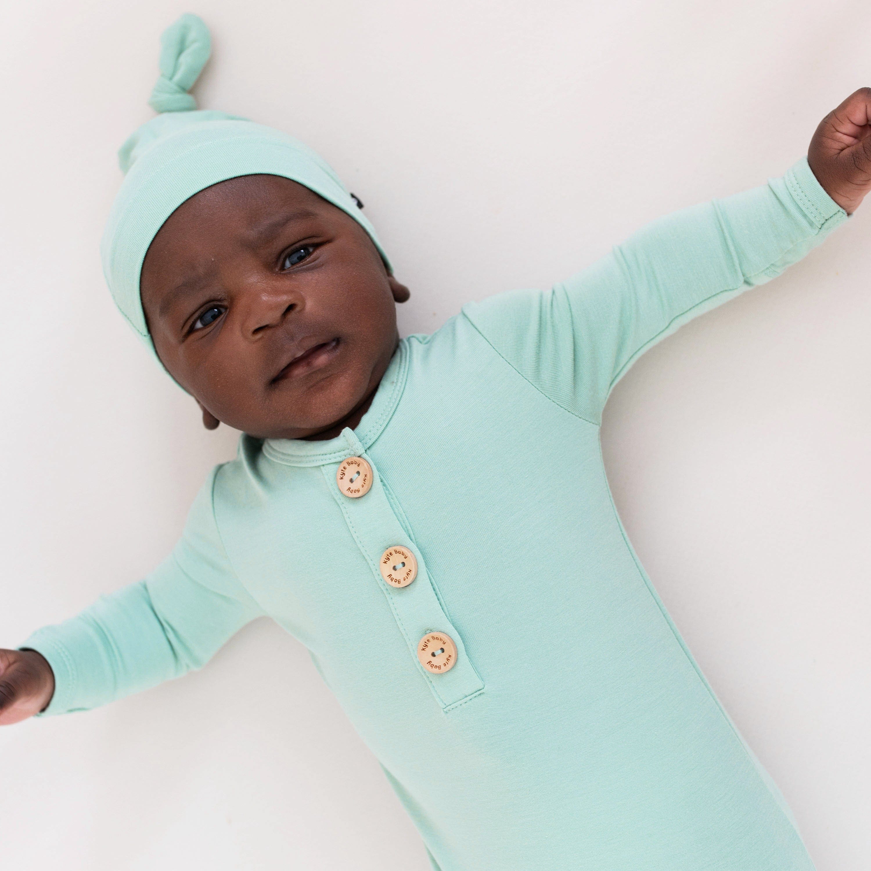 Infant wearing Kyte Baby bamboo Knotted Cap in Wasabi with matching gown