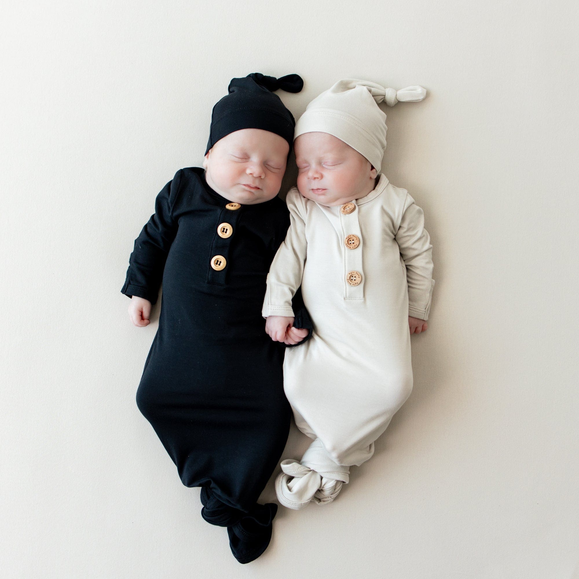 Sleeping newborns laying next to each other wearing Kyte Baby Knotted Gown with Hat Sets in Midnight and Oat