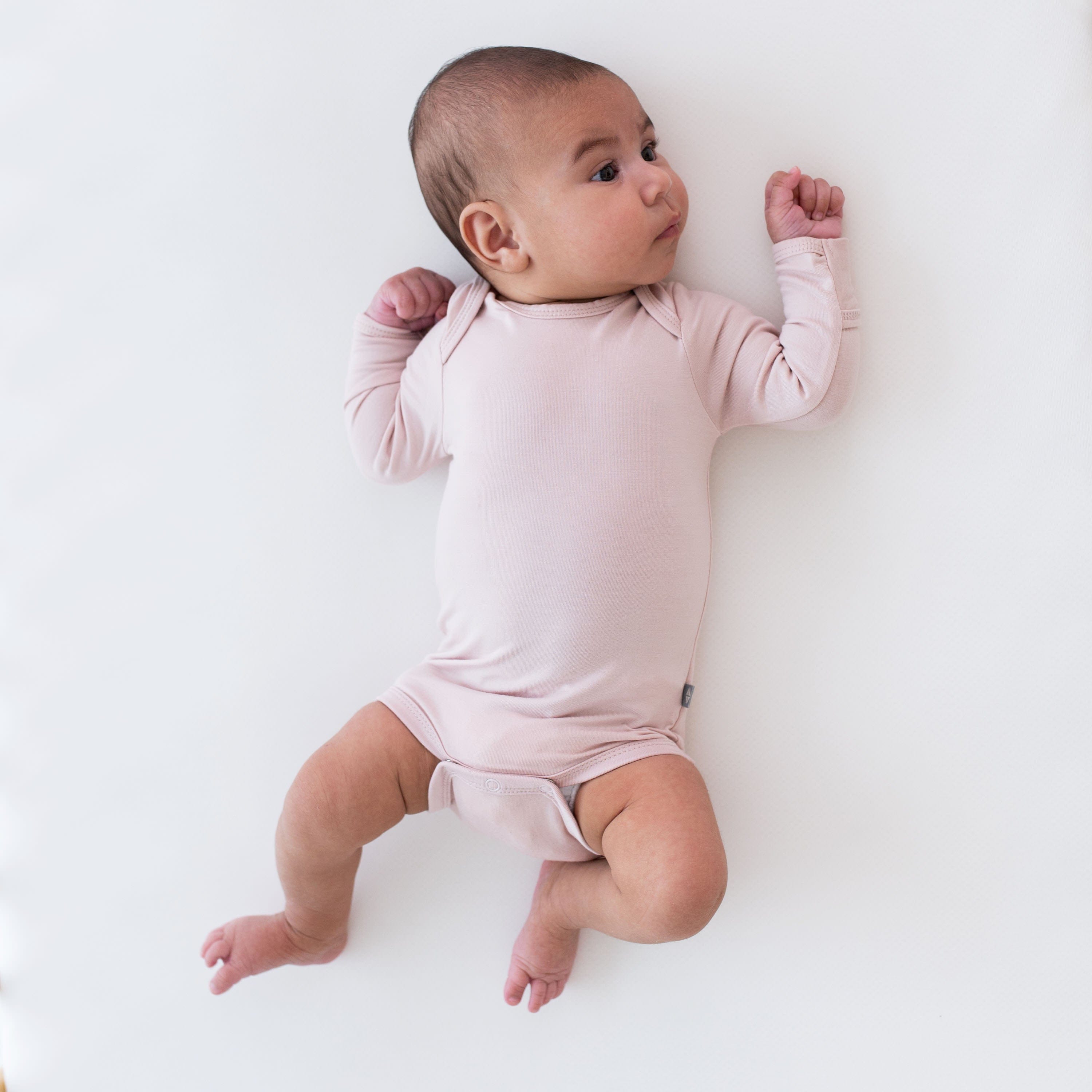Infant wearing Long Sleeve Bodysuit in Blush while laying on a white surface