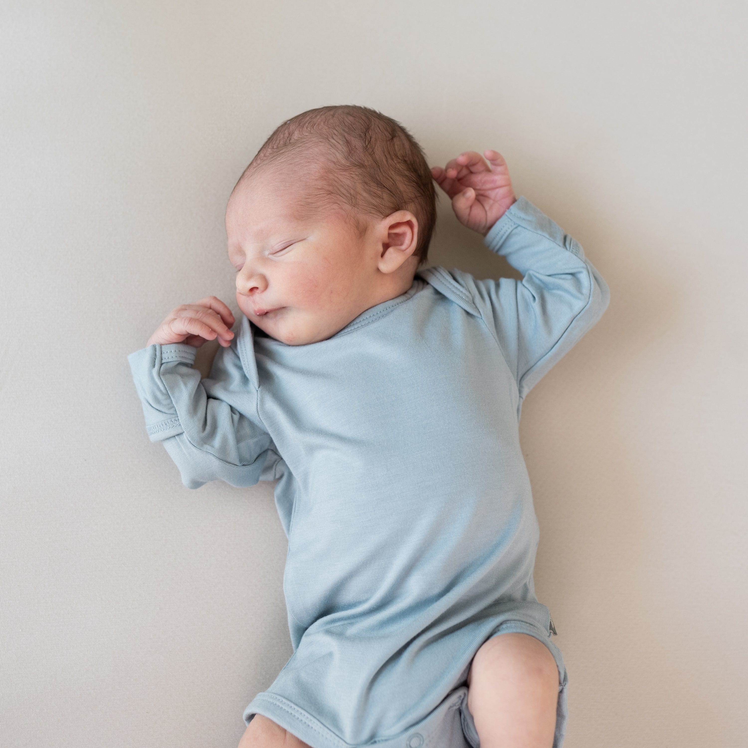 Sleeping newborn wearing Kyte Baby Long Sleeve Bodysuit in Fog