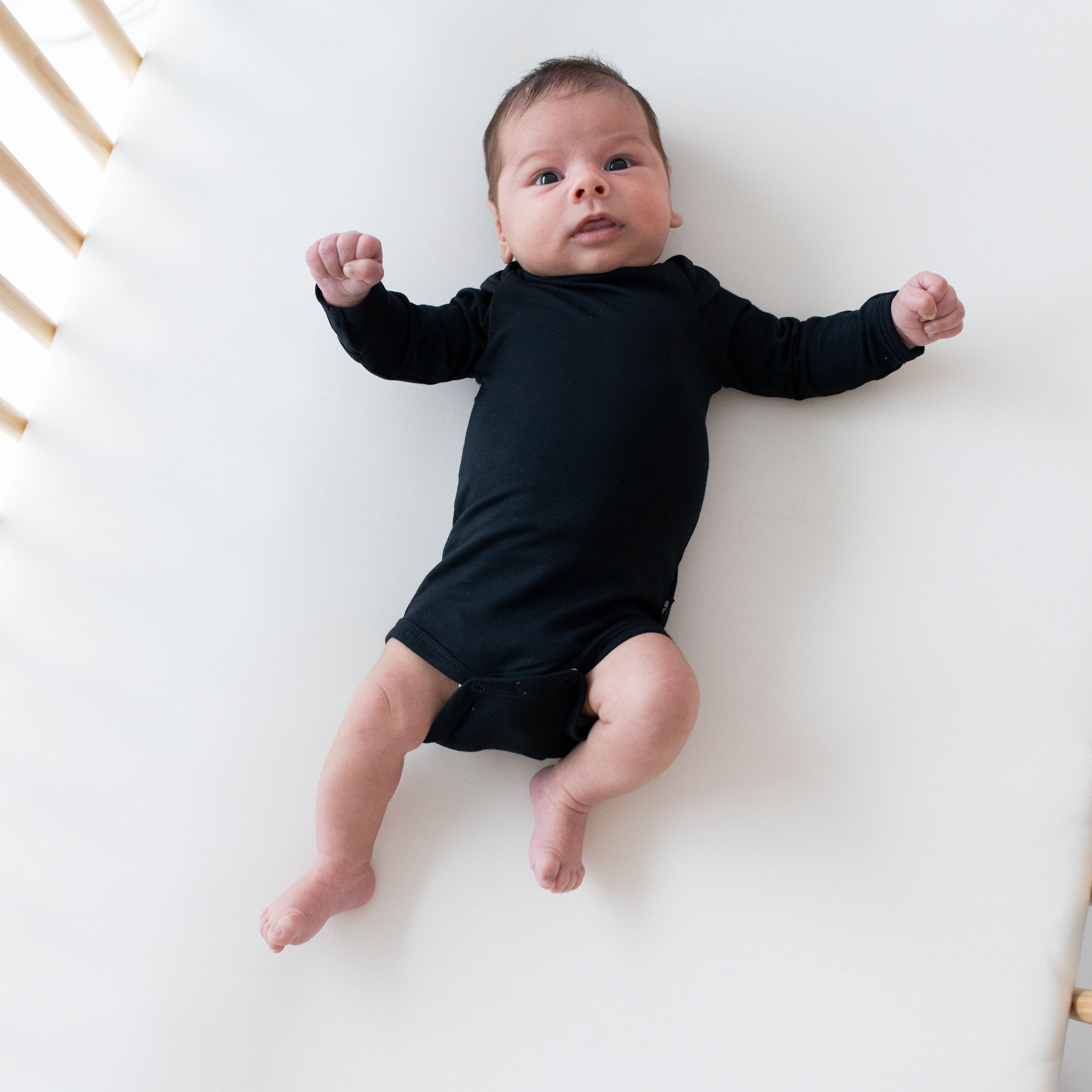 Baby laying in crib and wearing Kyte Baby Long Sleeve Bodysuit in Midnight