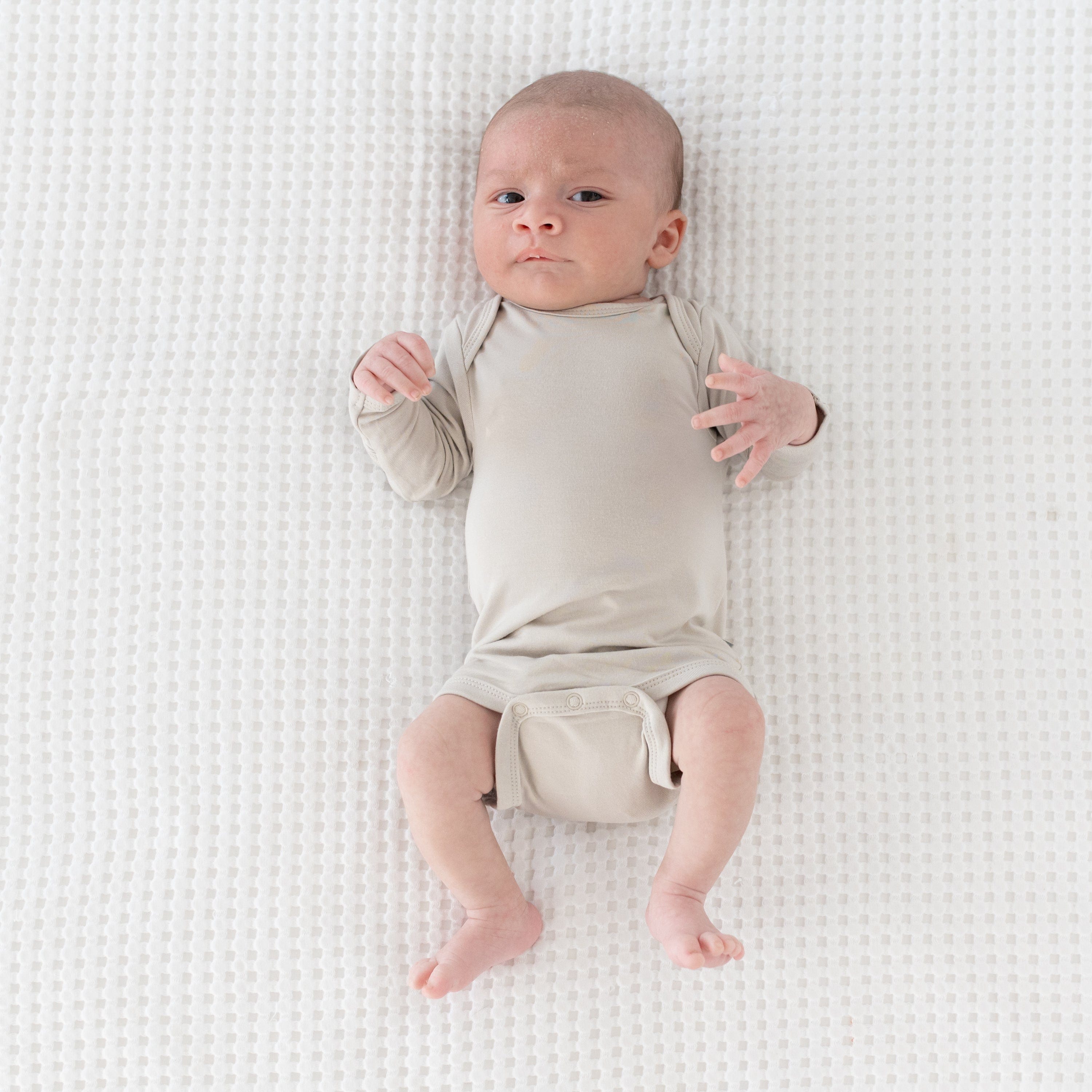 Newborn wearing Kyte Baby Long Sleeve Bodysuit in Oat