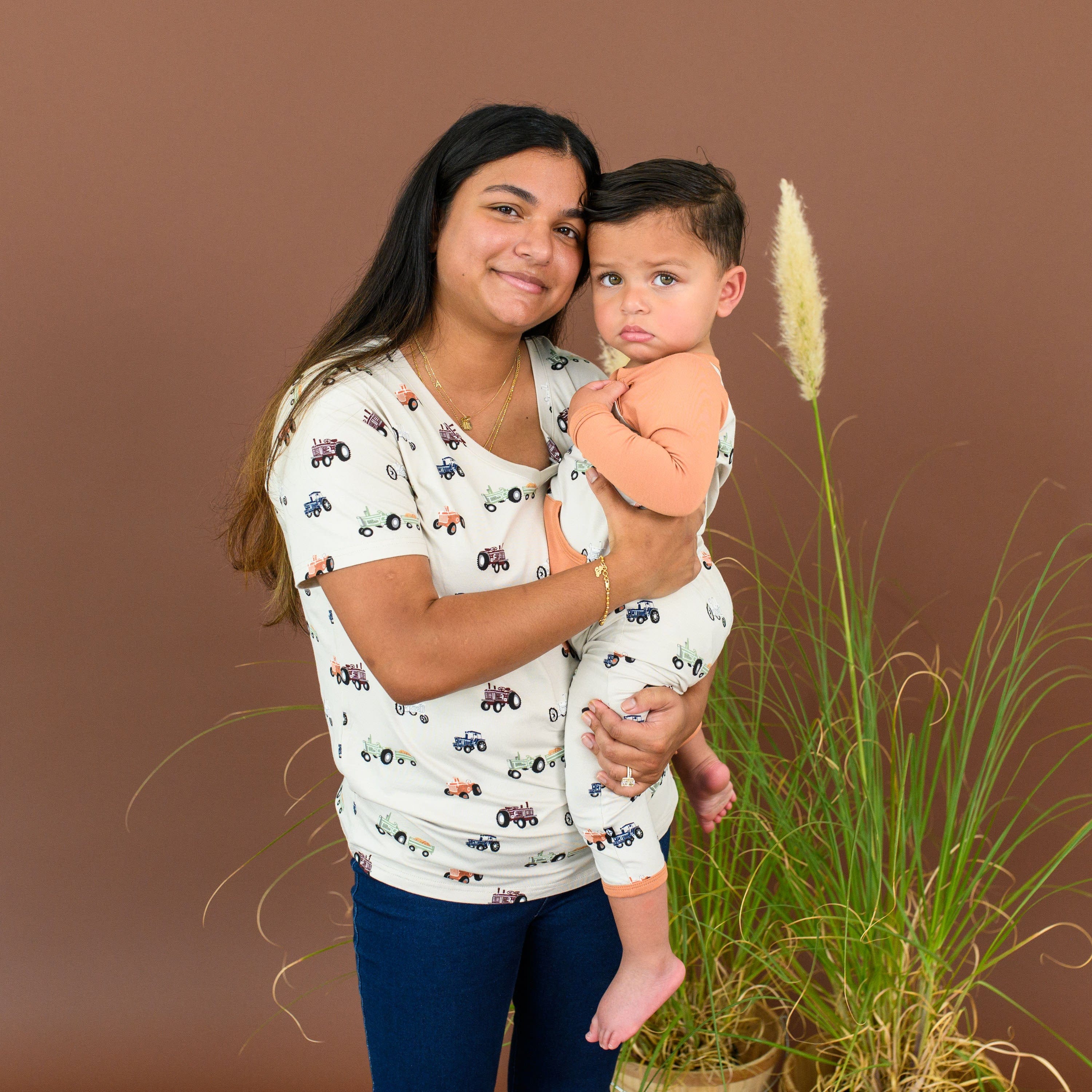 Woman wearing Kyte Baby Women's Relaxed Fit V-Neck in Tractor print holding Infant in matching Long Alls