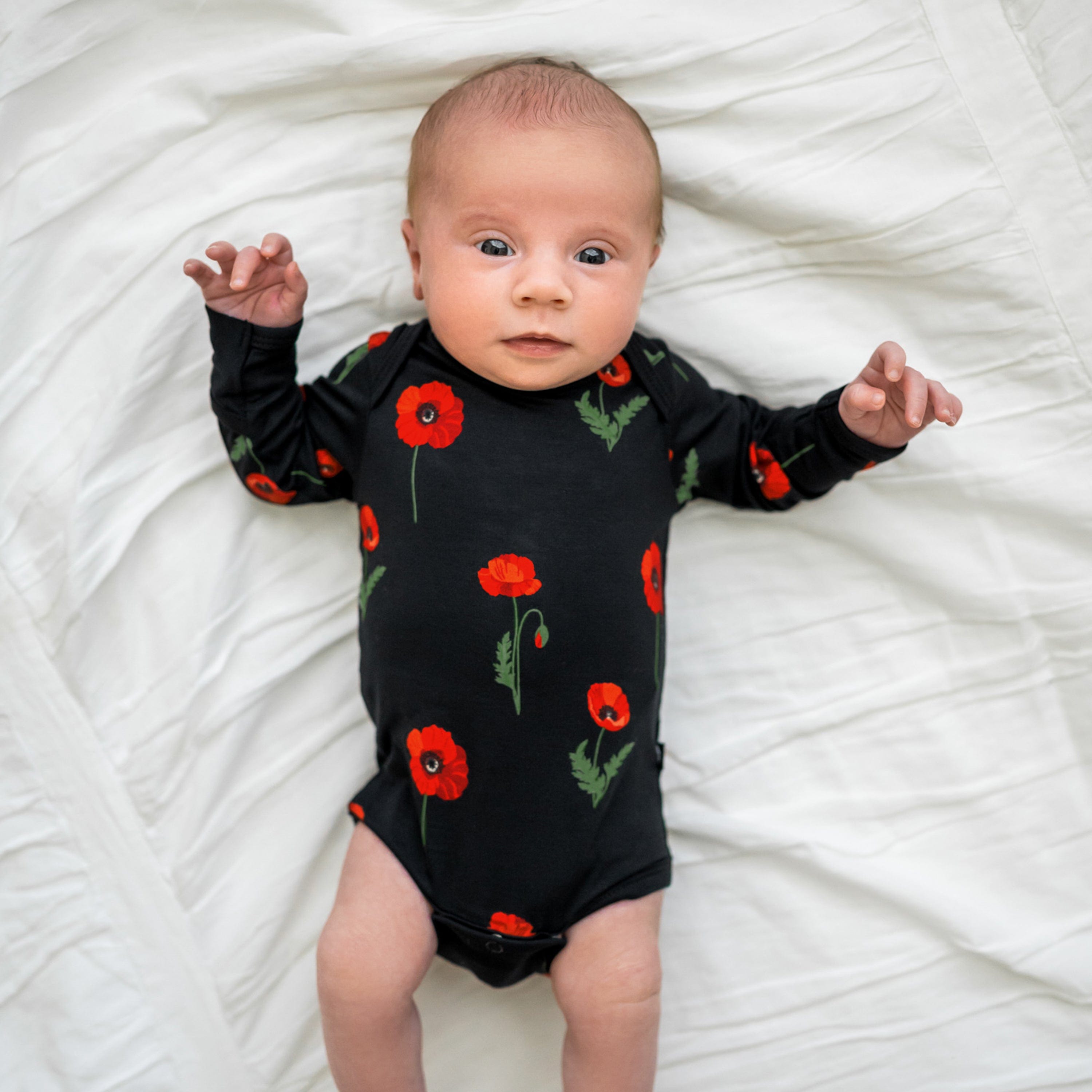 Infant wearing Kyte Baby Long Sleeve Bodysuit in Midnight Poppies