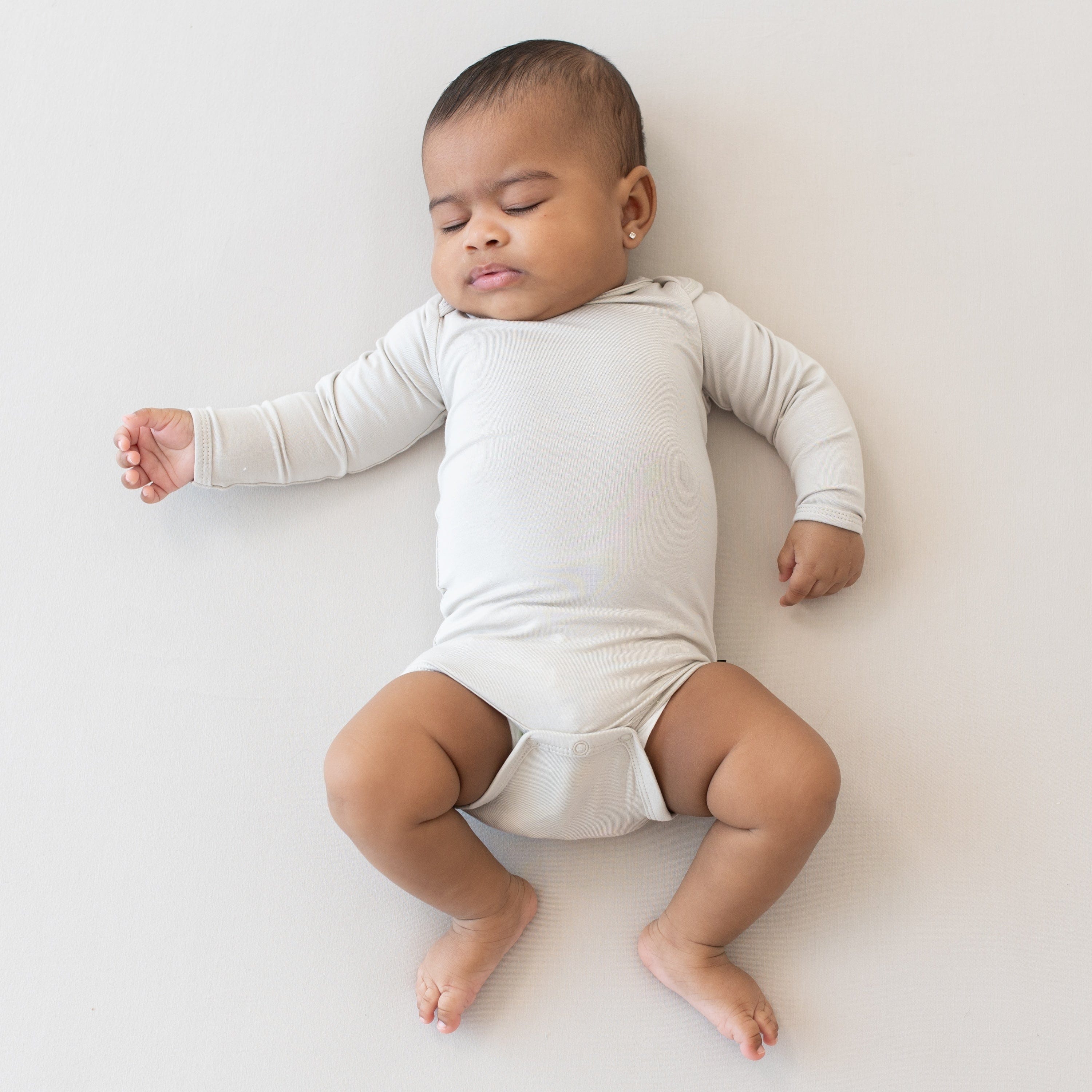 Sleeping infant laying on a Crib Sheet in Oat wearing a Kyte Baby Long Sleeve Bodysuit in Oat