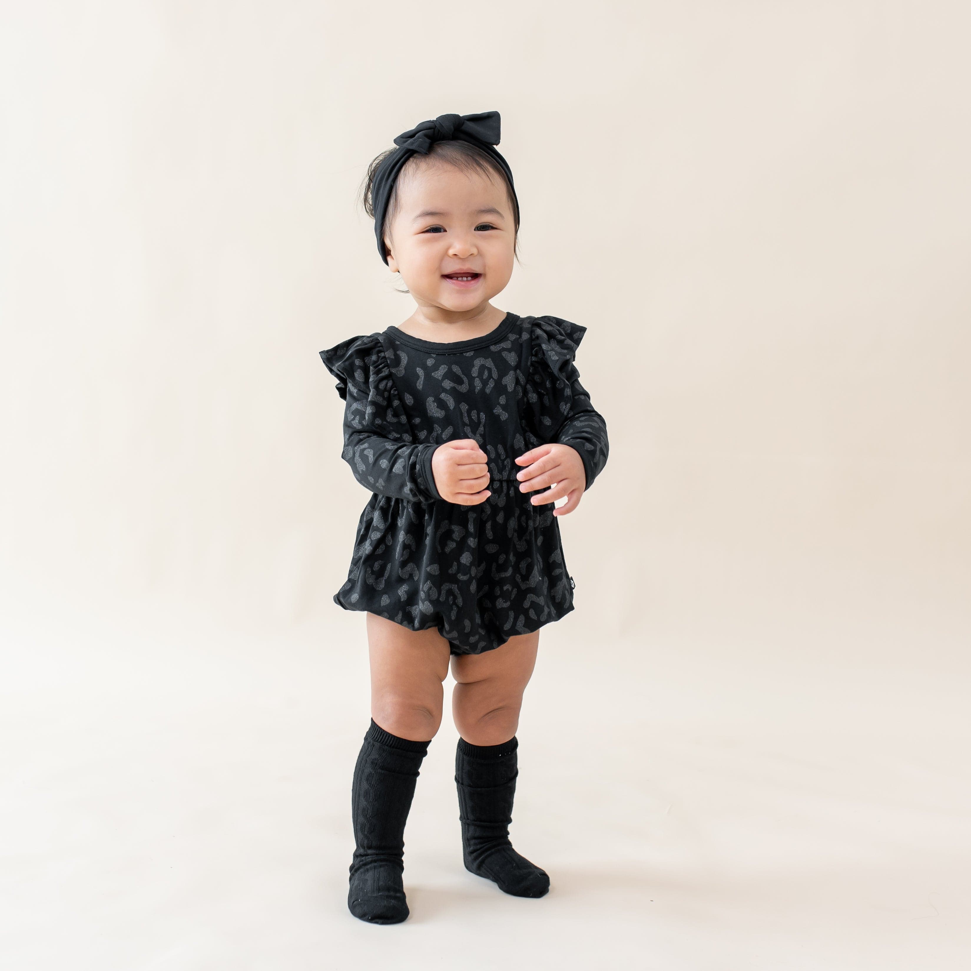 Toddler wearing Kyte Baby Long Sleeve Bubble Romper with ruffles in Midnight Leopard