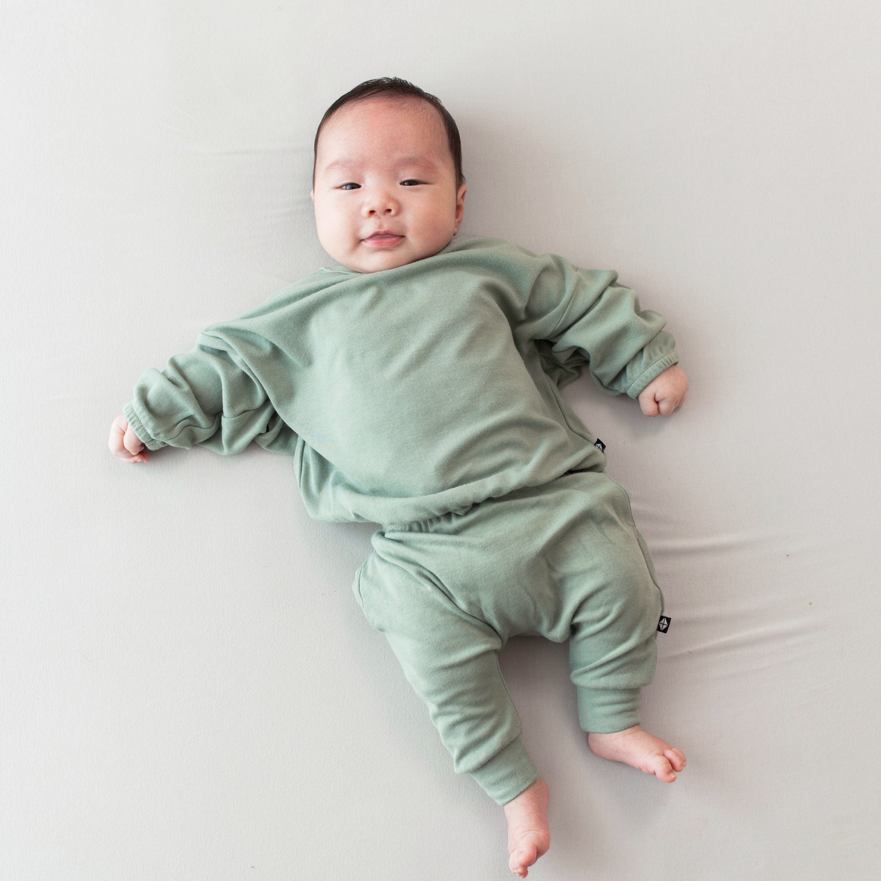 Infant wearing Kyte Baby Bamboo Jersey Drop Shoulder Top with Crew Neck in Thyme