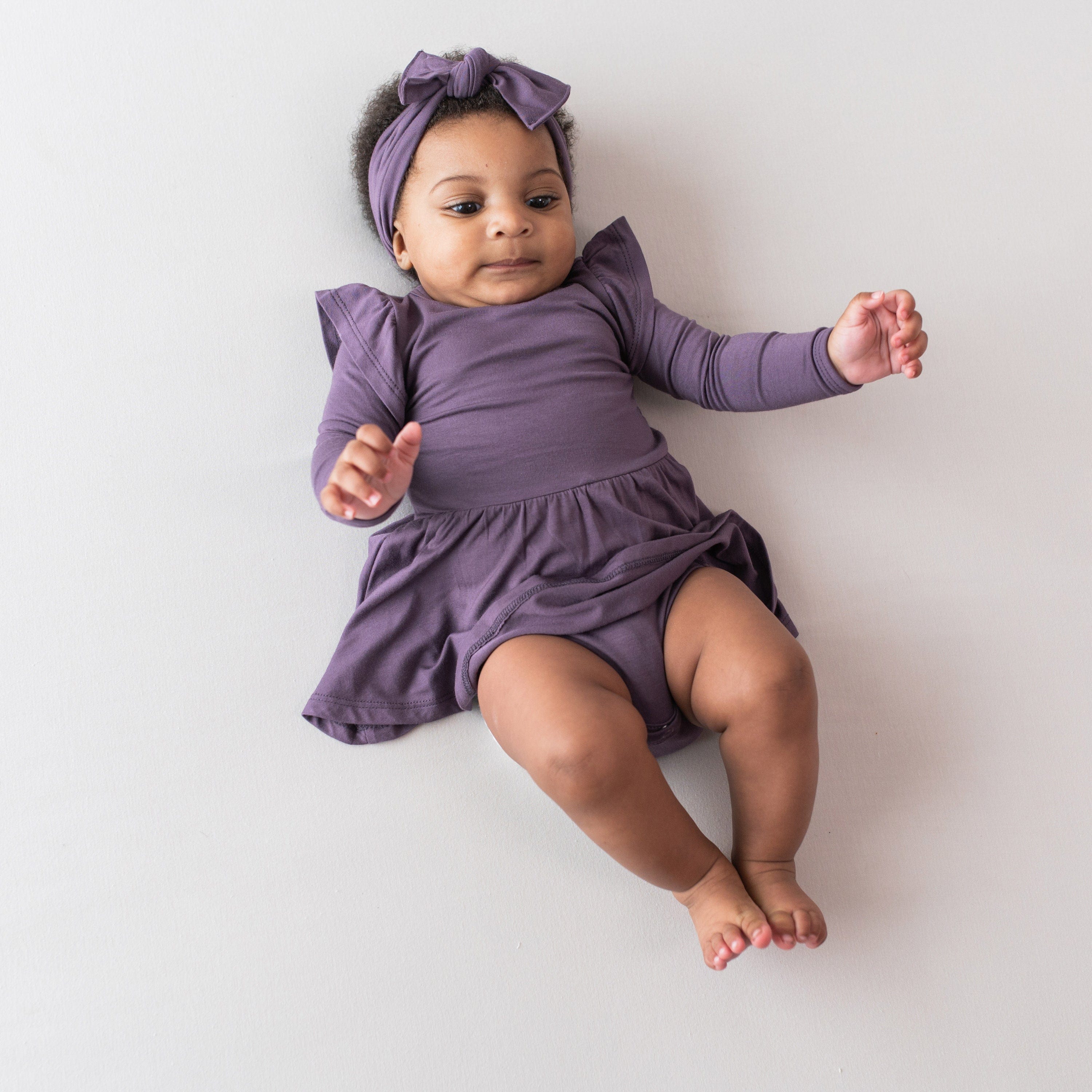 Infant wearing Kyte Baby Bodysuit with Twirl Skirt in Currant with matching bow