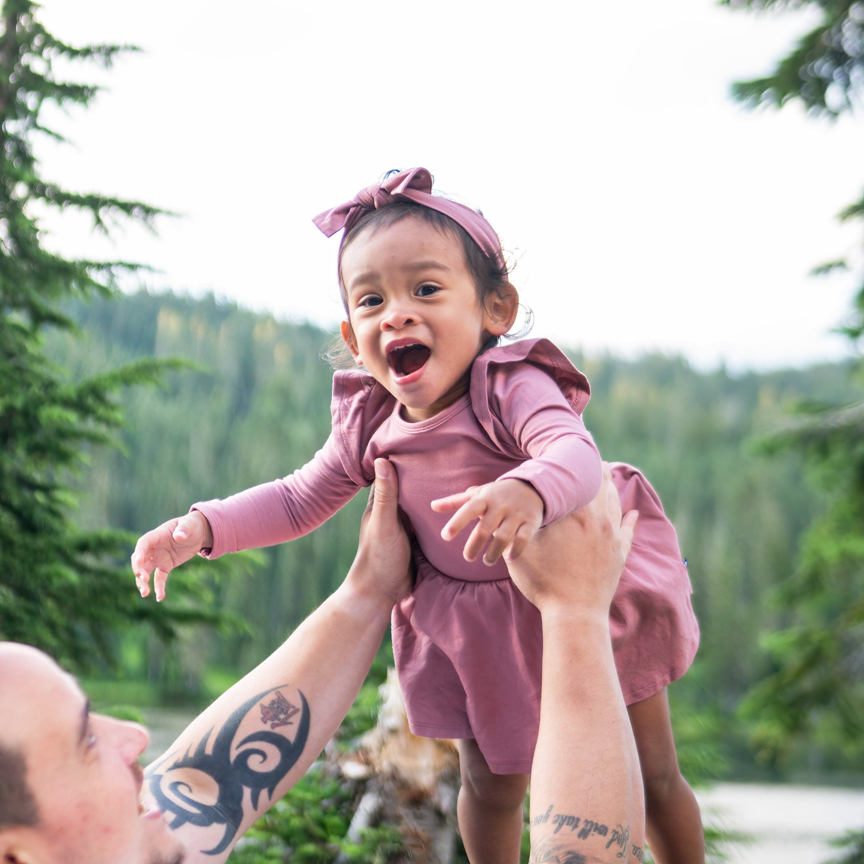 Girl wearing Kyte Baby bamboo Long Sleeve Twirl Bodysuit Infant Dress in Dusty Rose