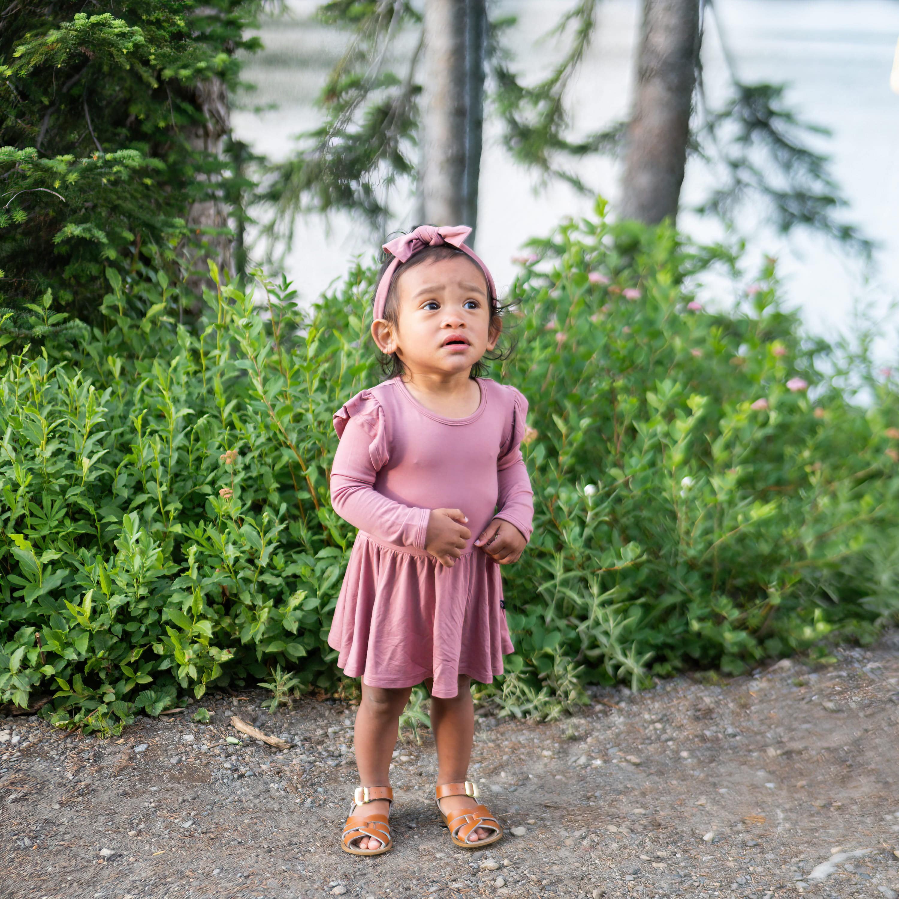 Child wearing Kyte Baby Long Sleeve infant Twirl Bodysuit Dress in Dusty Rose