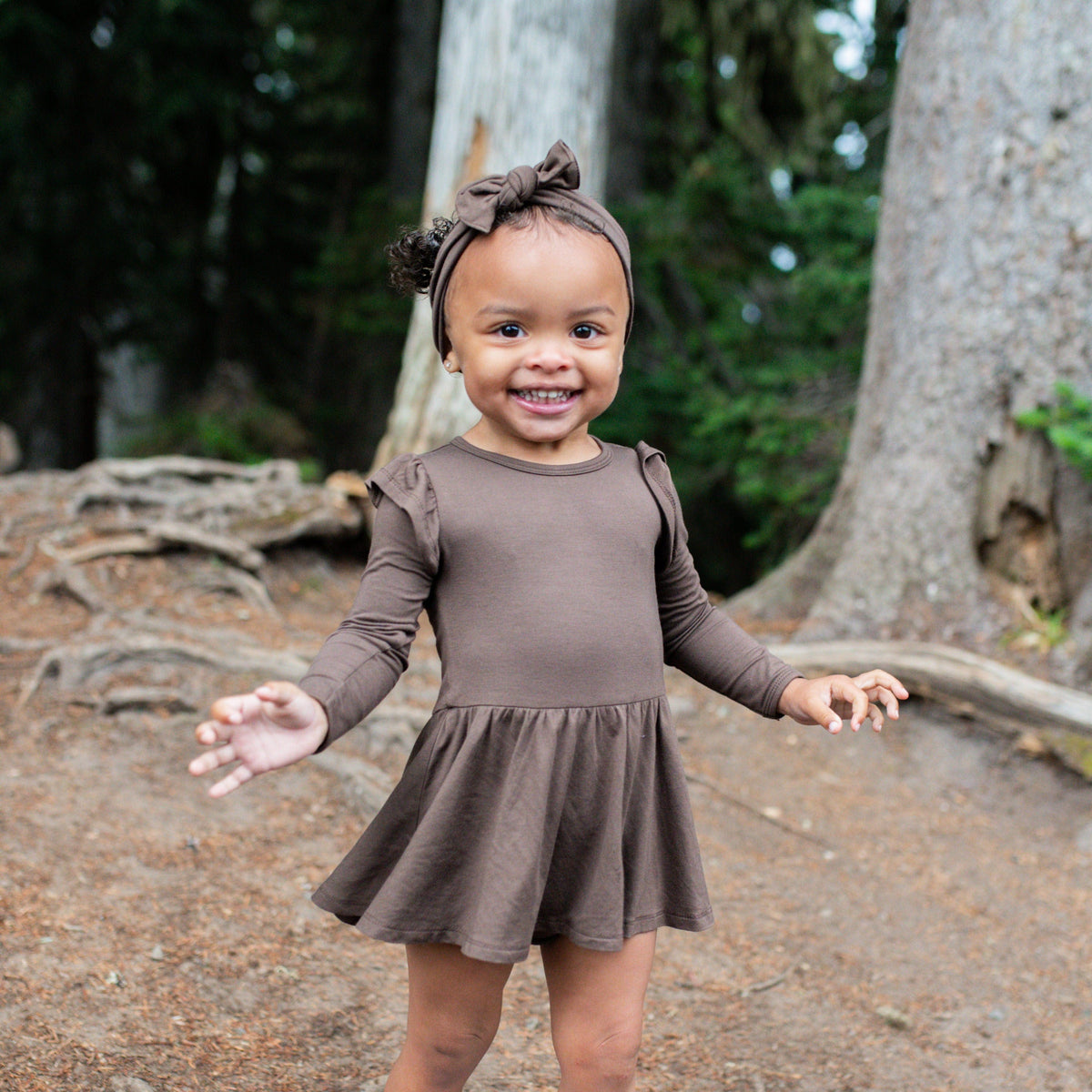 Toddler girl wearing the Long Sleeve Twirl Bodysuit Dress in Espresso with matching knotted bow headband
