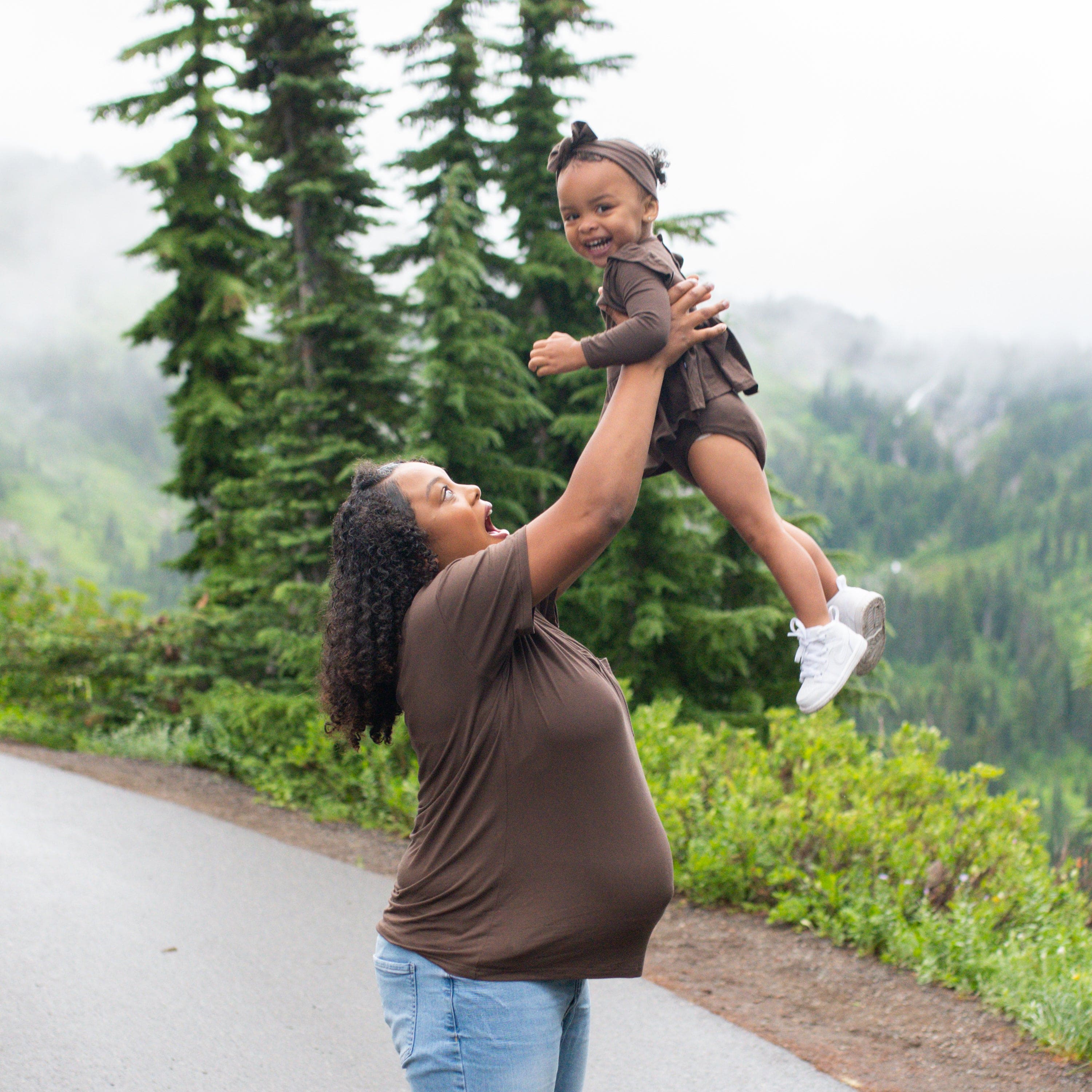 Toddler girl wearing the Long Sleeve Twirl Bodysuit Dress in Espresso being lifted in the air by her mother who is wearing a matching women's v-neck