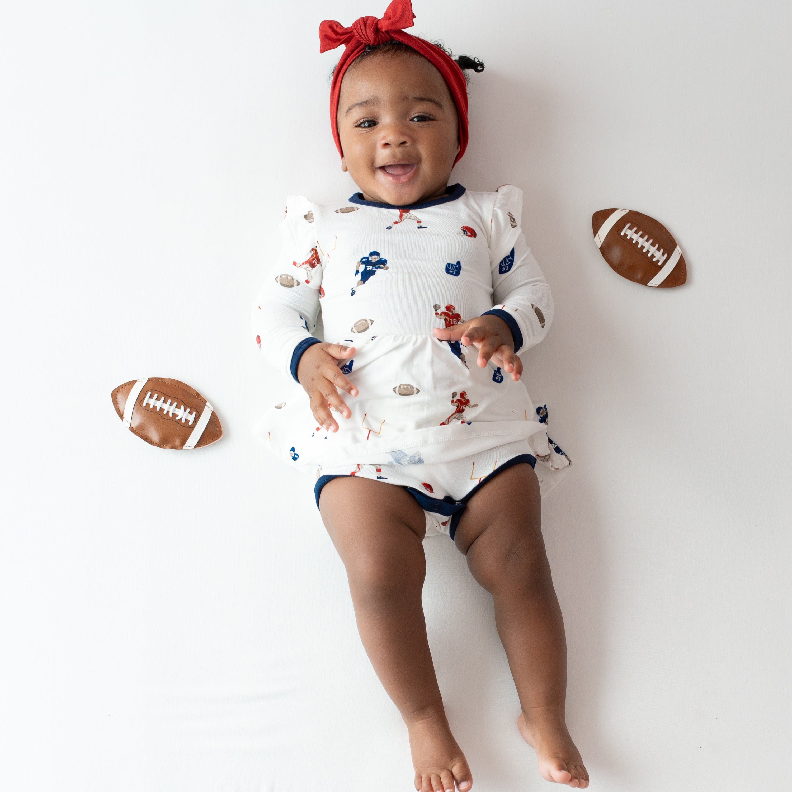 Infant wearing Kyte Baby Twirl Bodysuit Dress in Football