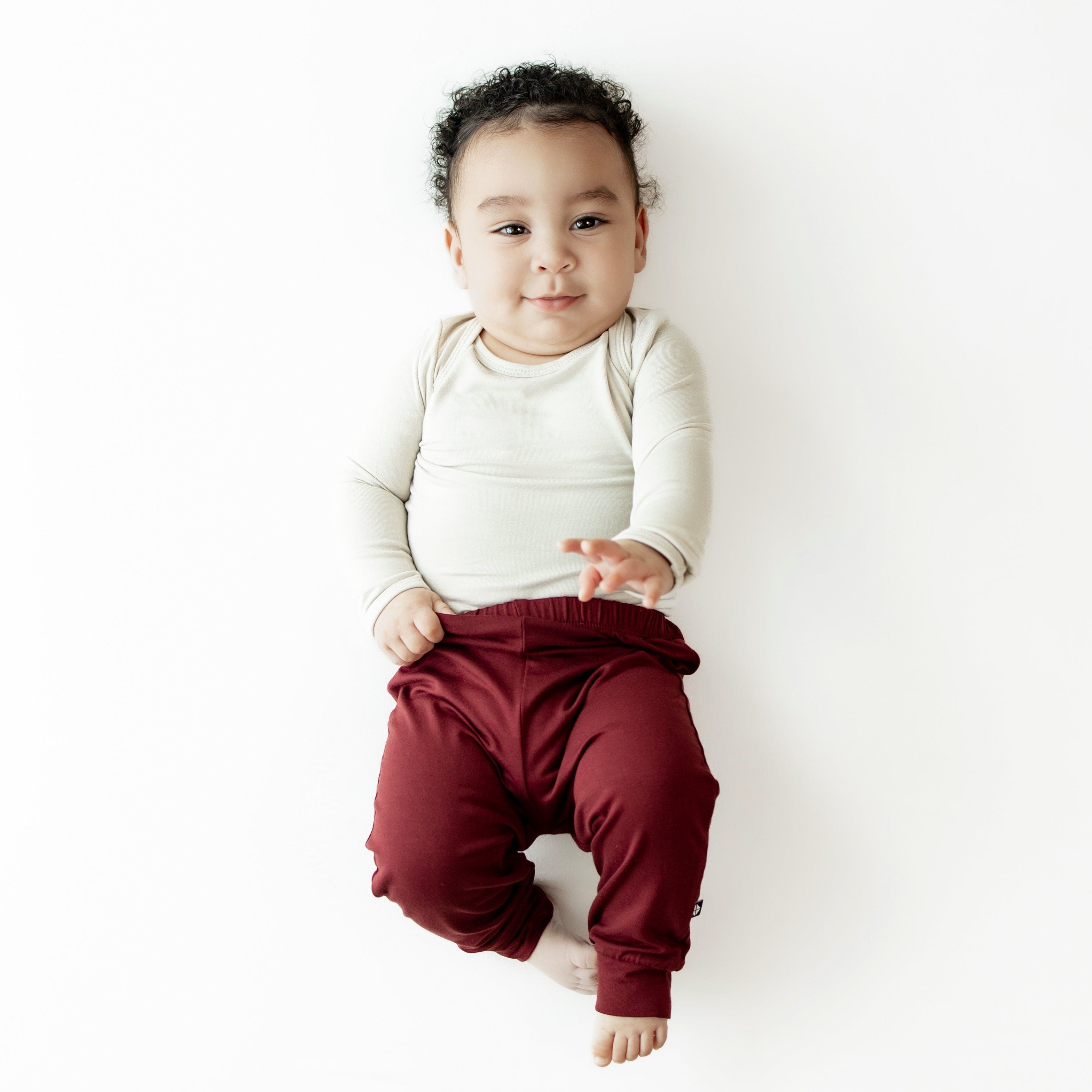 Baby model wearing the Pant in Burgundy paired with an Oat long sleeve bodysuit