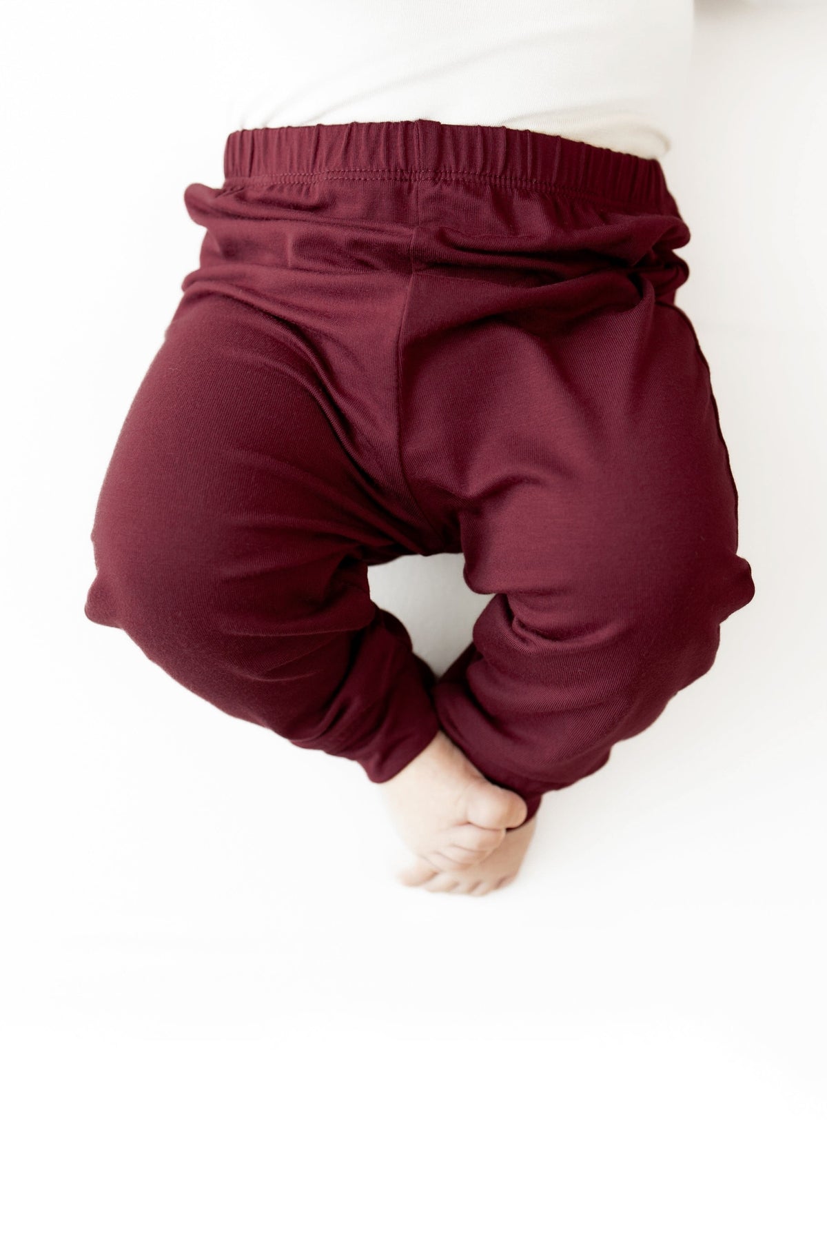 A close-up of a baby wearing burgundy elastic-waist pants, shown from the back against a plain white background.