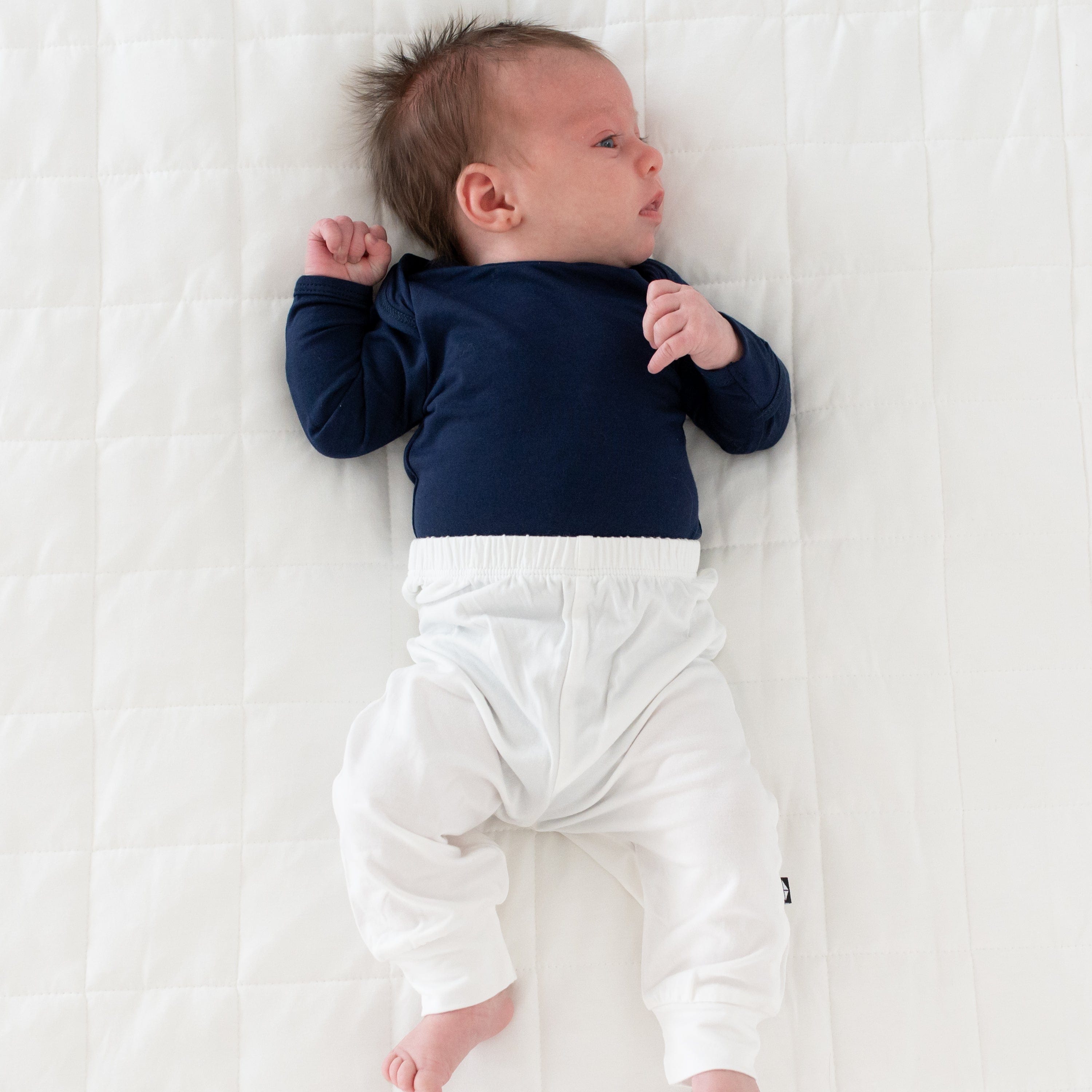 Newborn laying on white background wearing Kyte Baby Pant in Cloud white