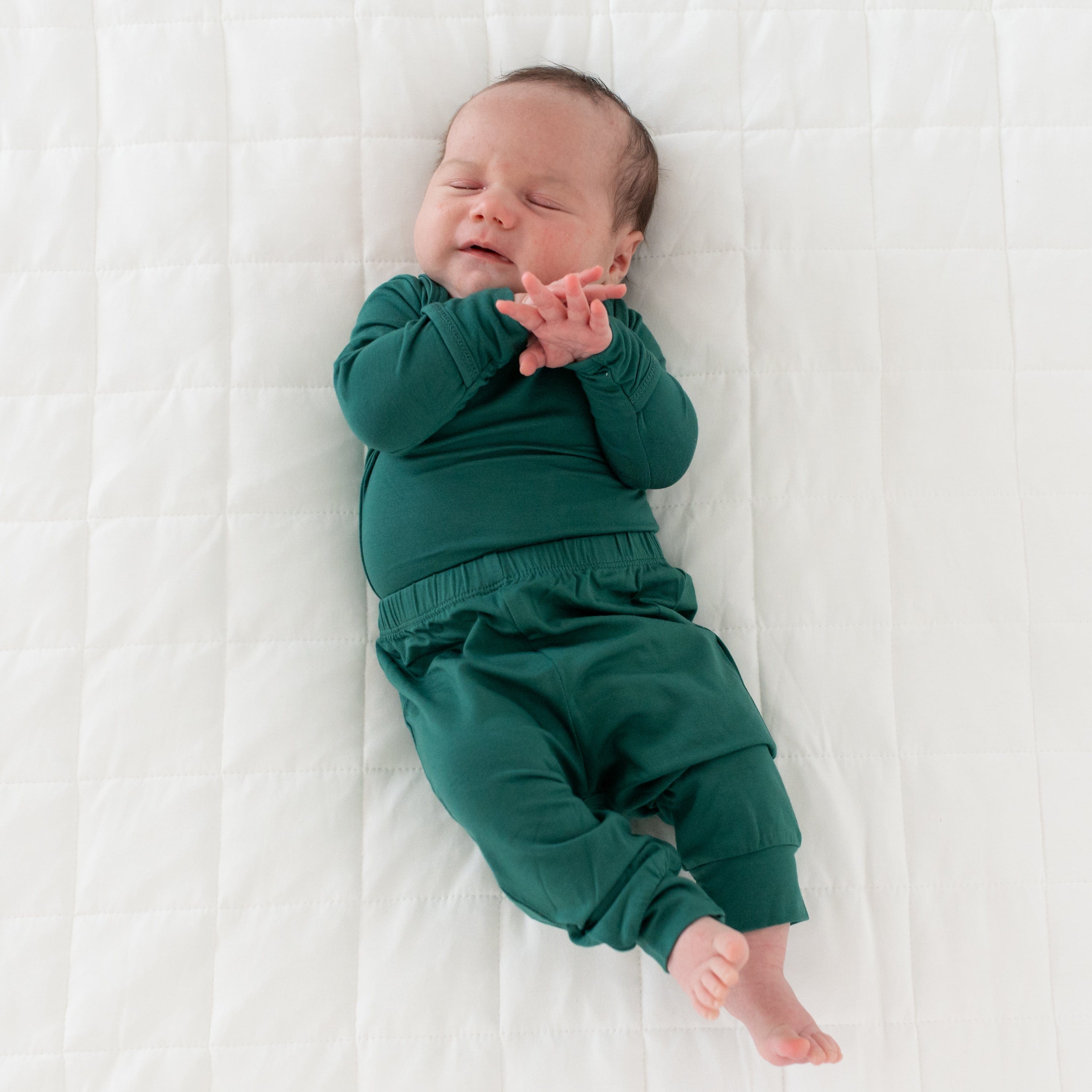 Sleeping newborn laying on the quilted side of a Cloud blanket and wearing Kyte Baby Pants in Emerald