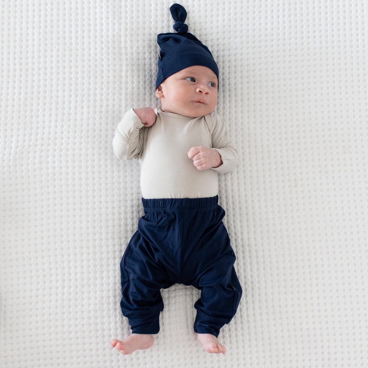 Newborn wearing Kyte Baby Pants in Navy with matching knotted hat