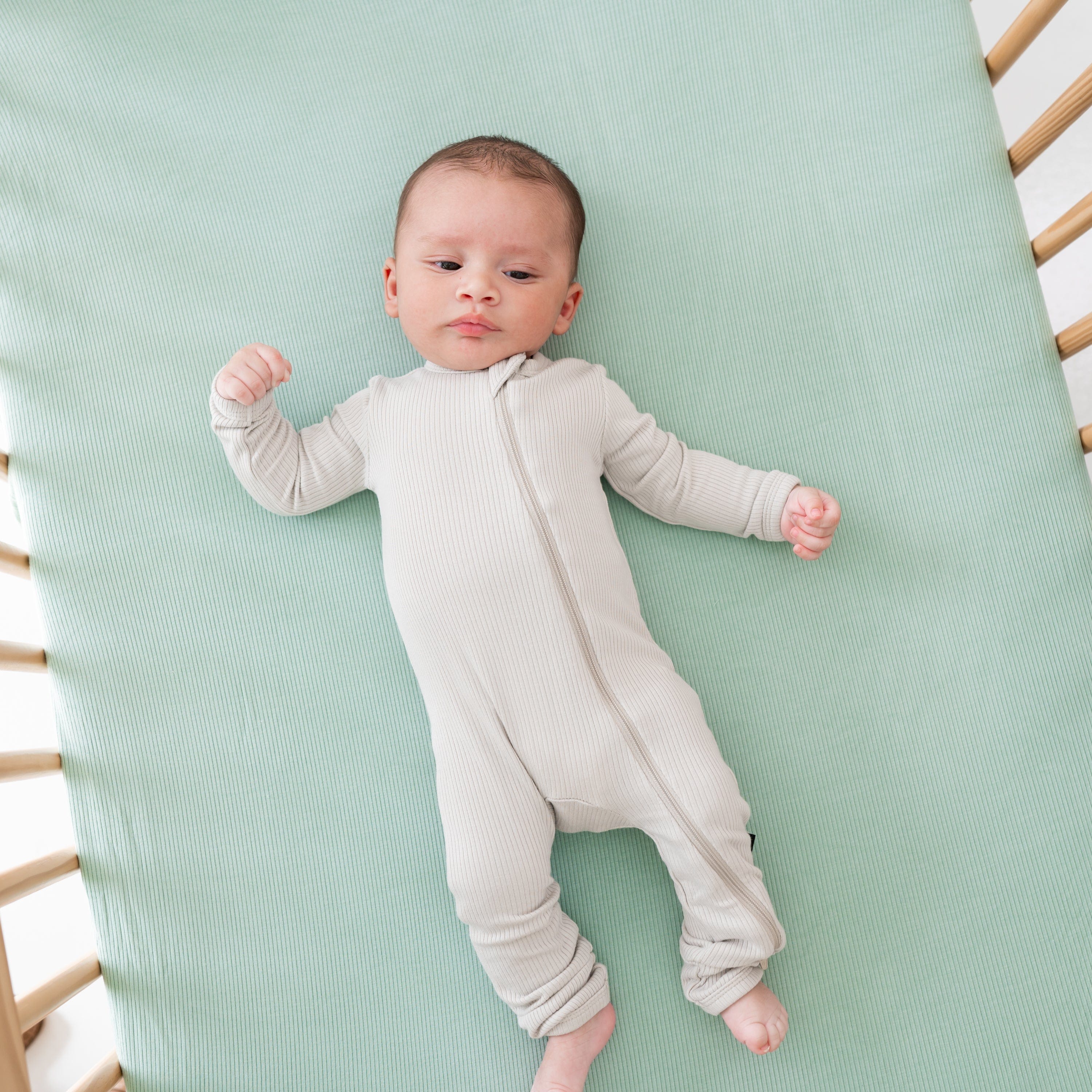 Newborn laying on Kyte Baby Ribbed Crib Sheet in Sage