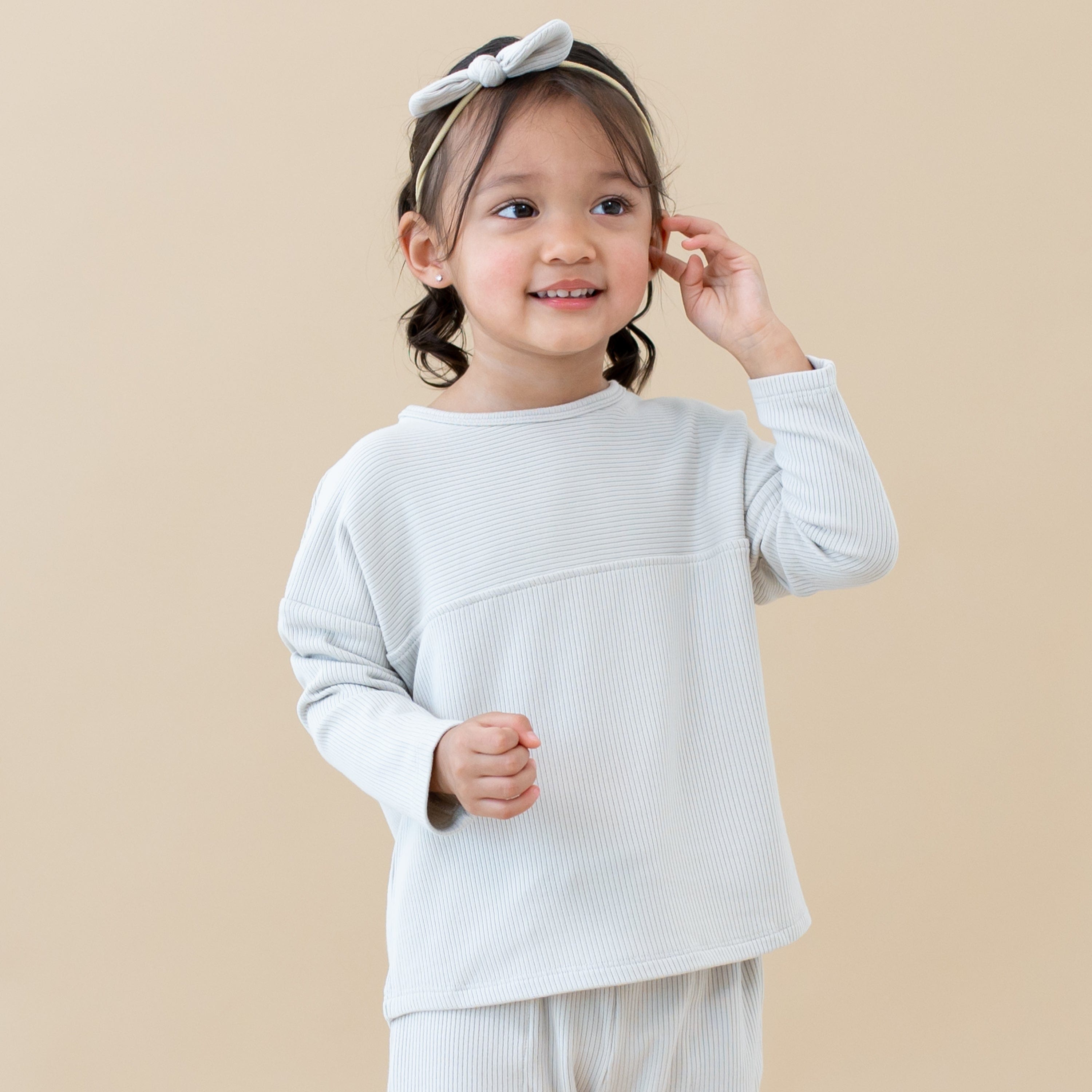Toddler wearing Kyte Baby Ribbed Drop Shoulder Top in Oat with matching Nylon Bow