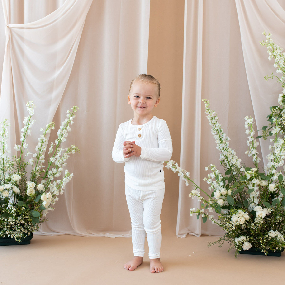 Toddler wearing Kyte Baby Ribbed Henley Set in Cloud. Toddler is standing between two floral bushes
